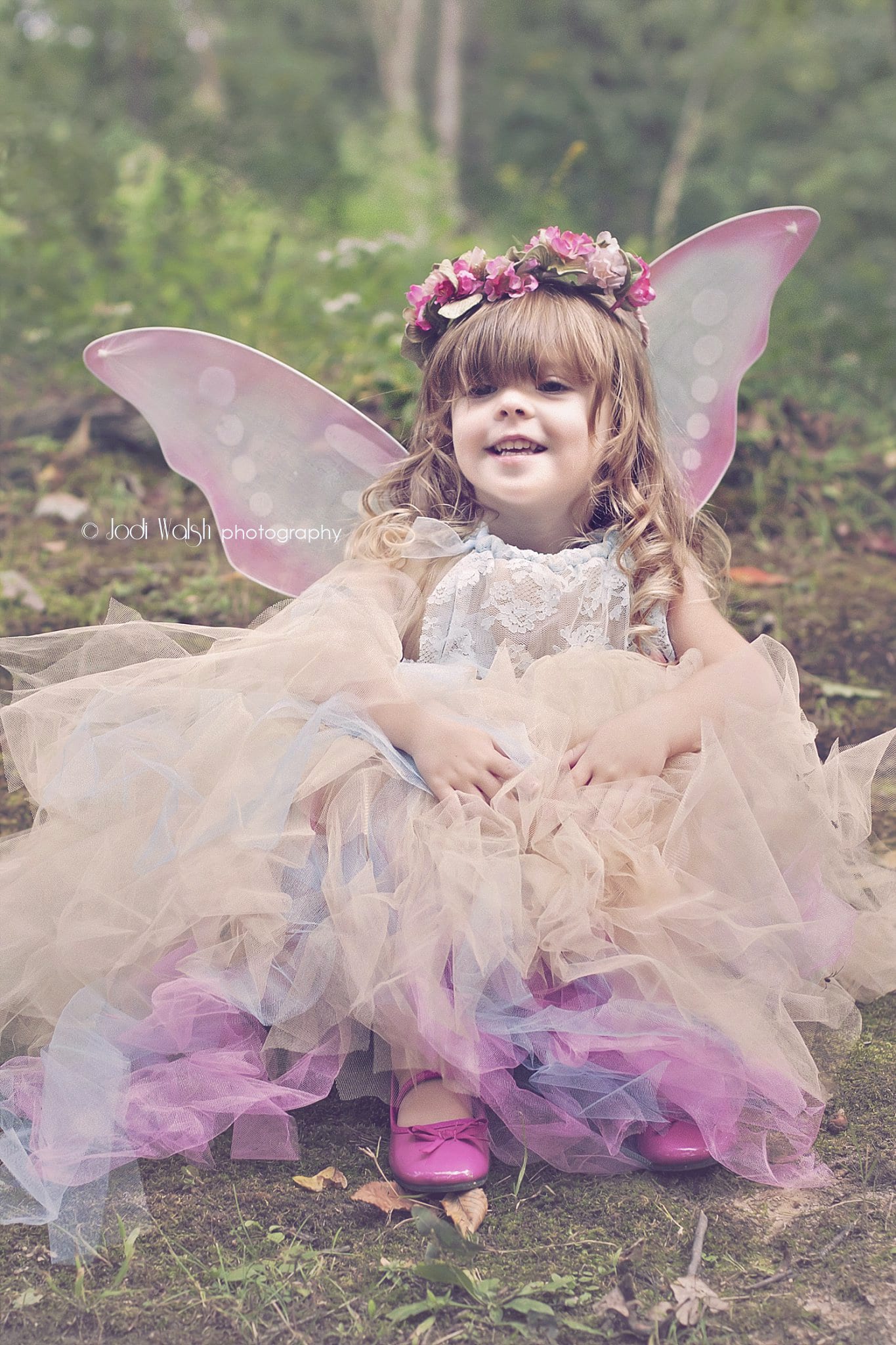 little girl sitting in the woods wearing fairy dress with crown and wings