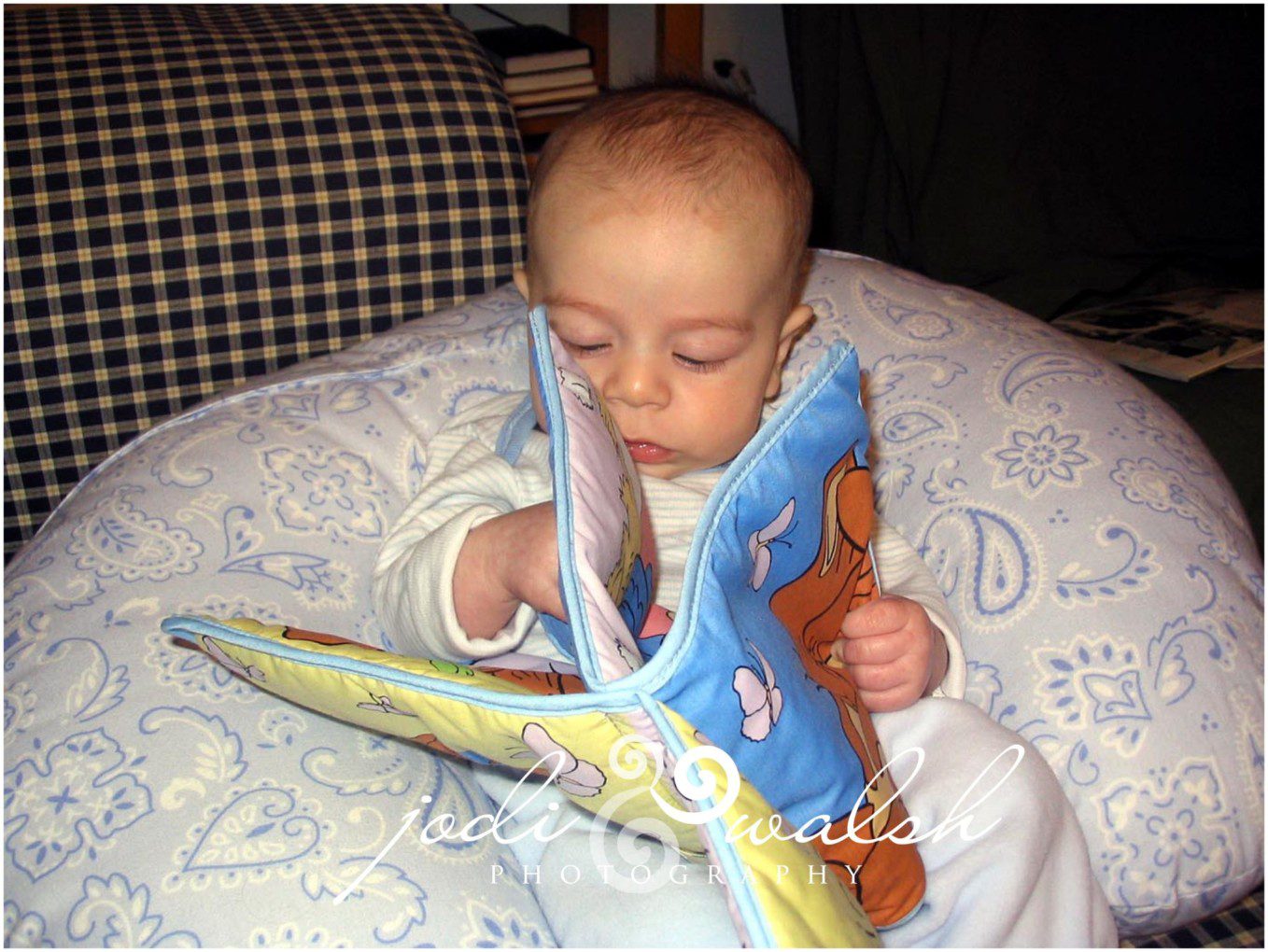 baby sitting in a boppy pillow looking at a cloth book