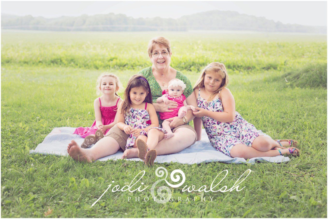 grandmother sitting in the grass surrounded by her four granddaughters