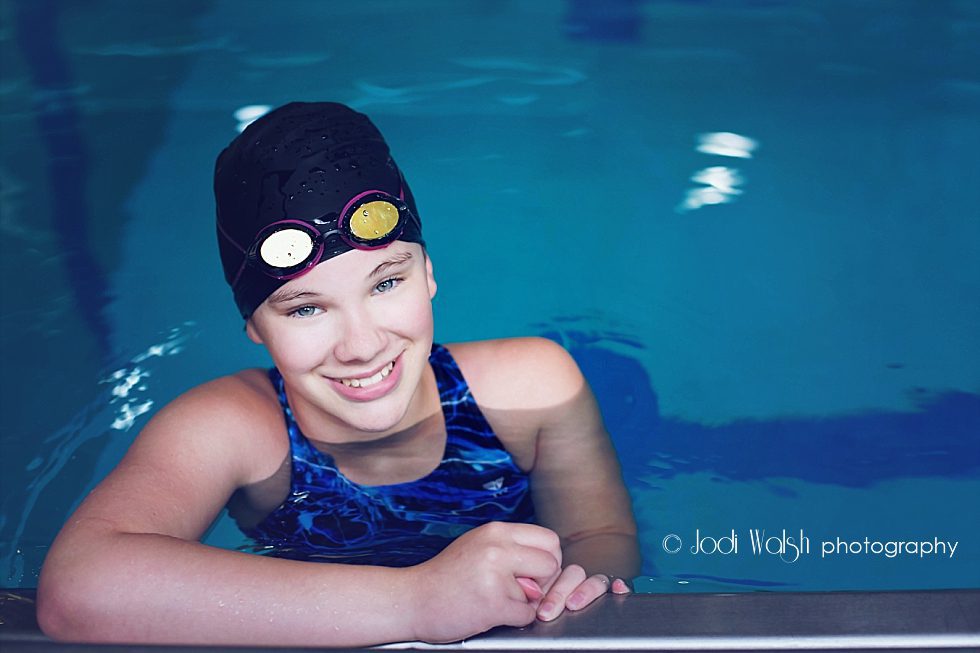 Pittsburgh tween swimmer in pool smiling with goggles on her forehead 