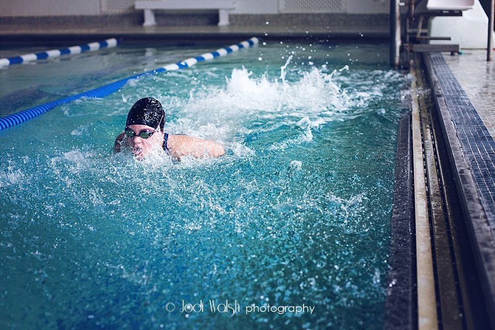 image of a swimmer swimming in the lane of the pool at the Sewickley YMCA. She's wearing a black cap and goggles and is popping up to take a breath.