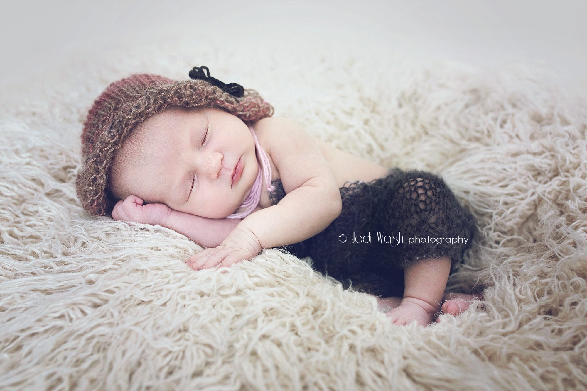 newborn sleeping on hand in knit romper and bonnet