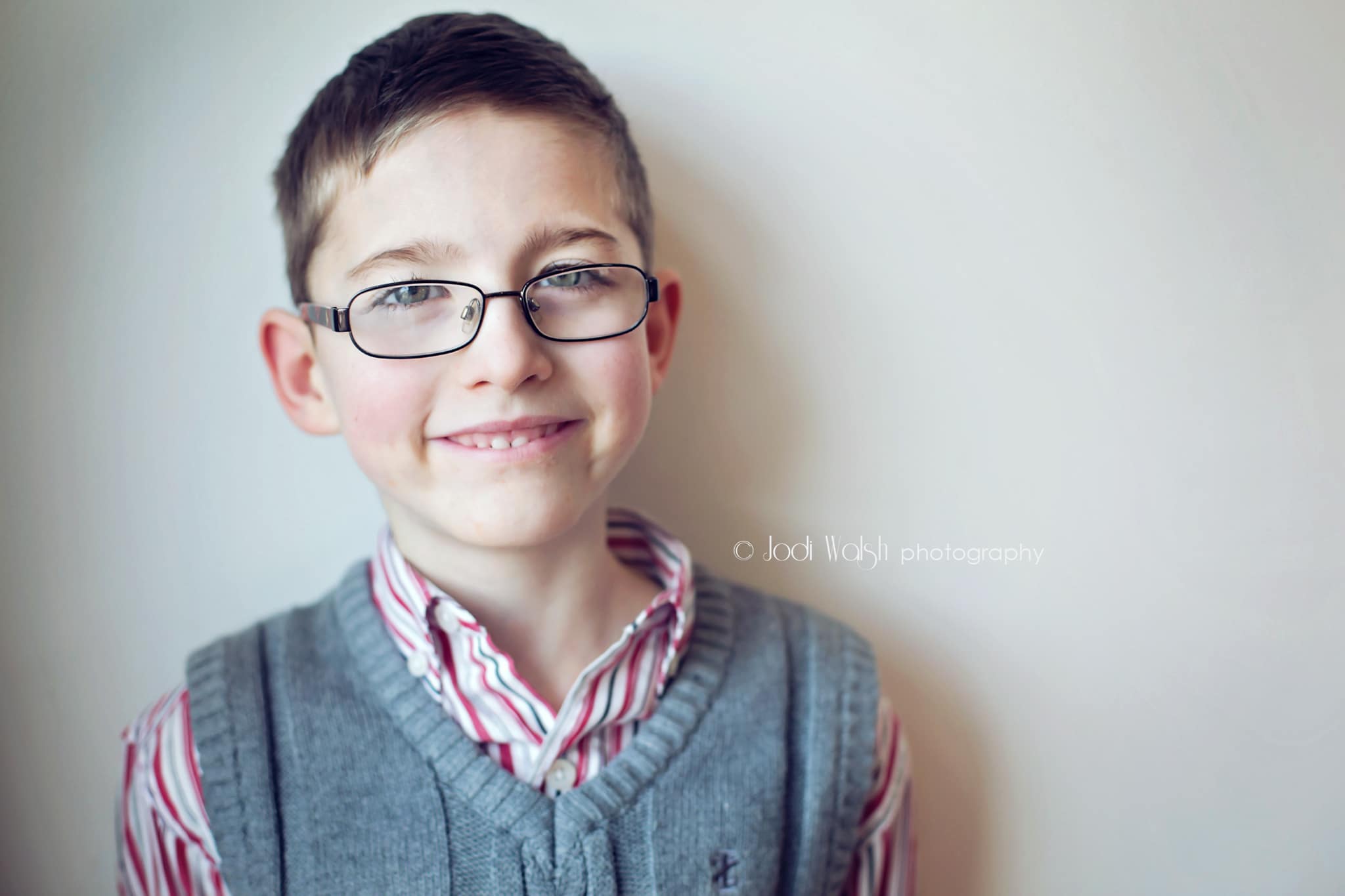 boy with glasses in gray sweater vest and red plaid shirt
