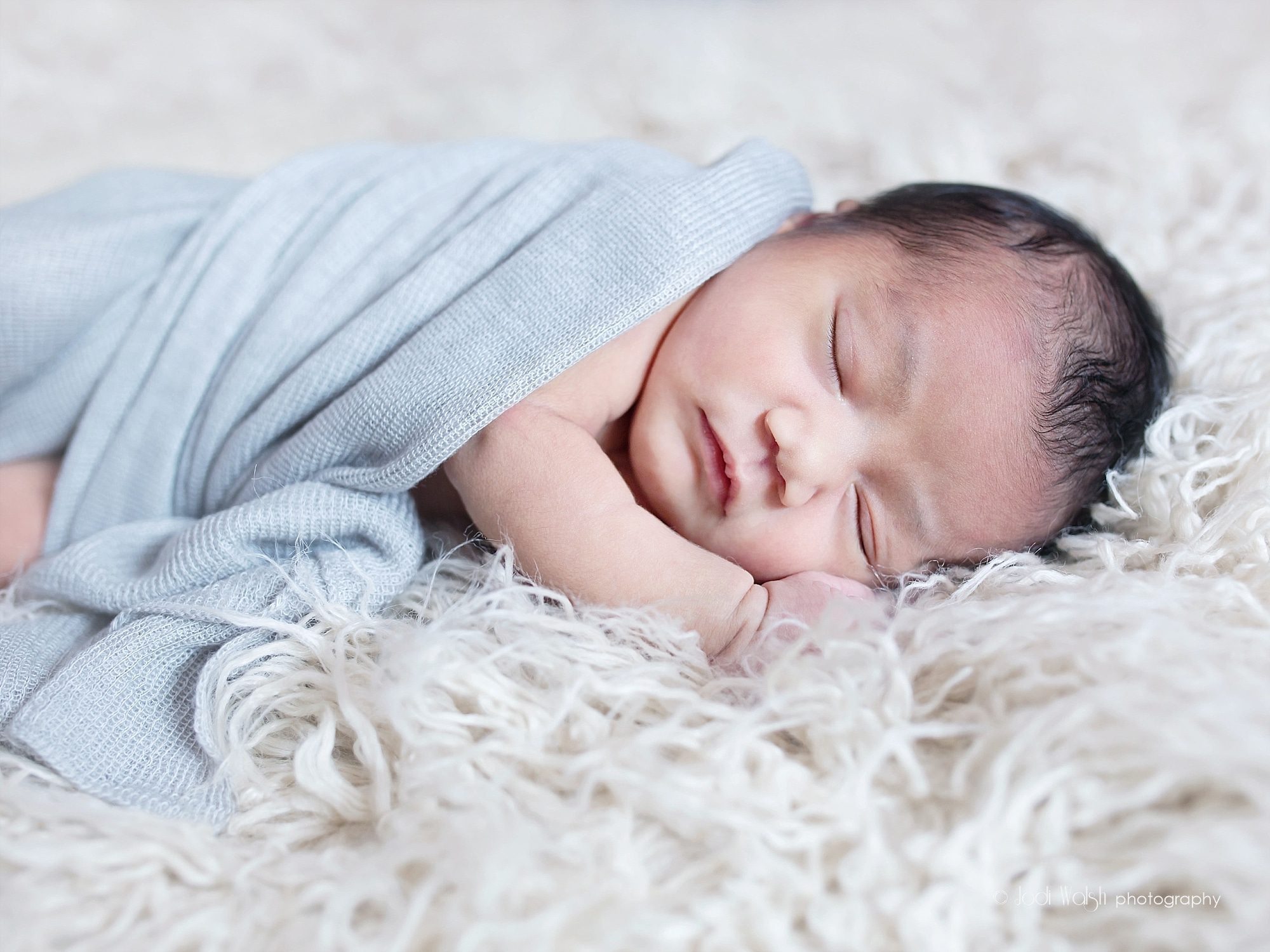 newborn baby girl with dark hair wrapped in light gray wrap