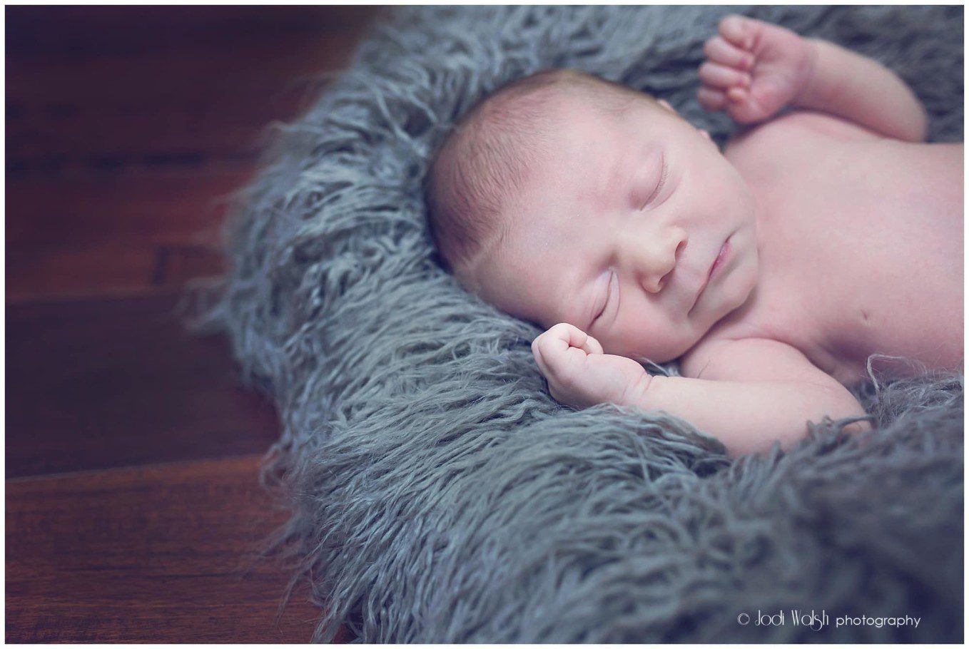 image of a newborn baby boy sleeping on a gray blue fuzzy blanket.