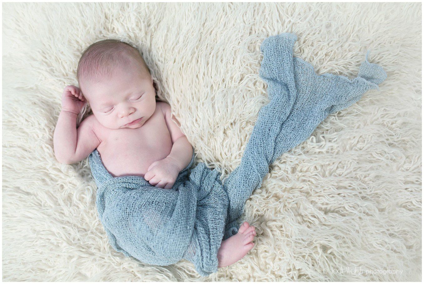 image of a newborn baby boy sleeping on cream fur with gray blue wrap