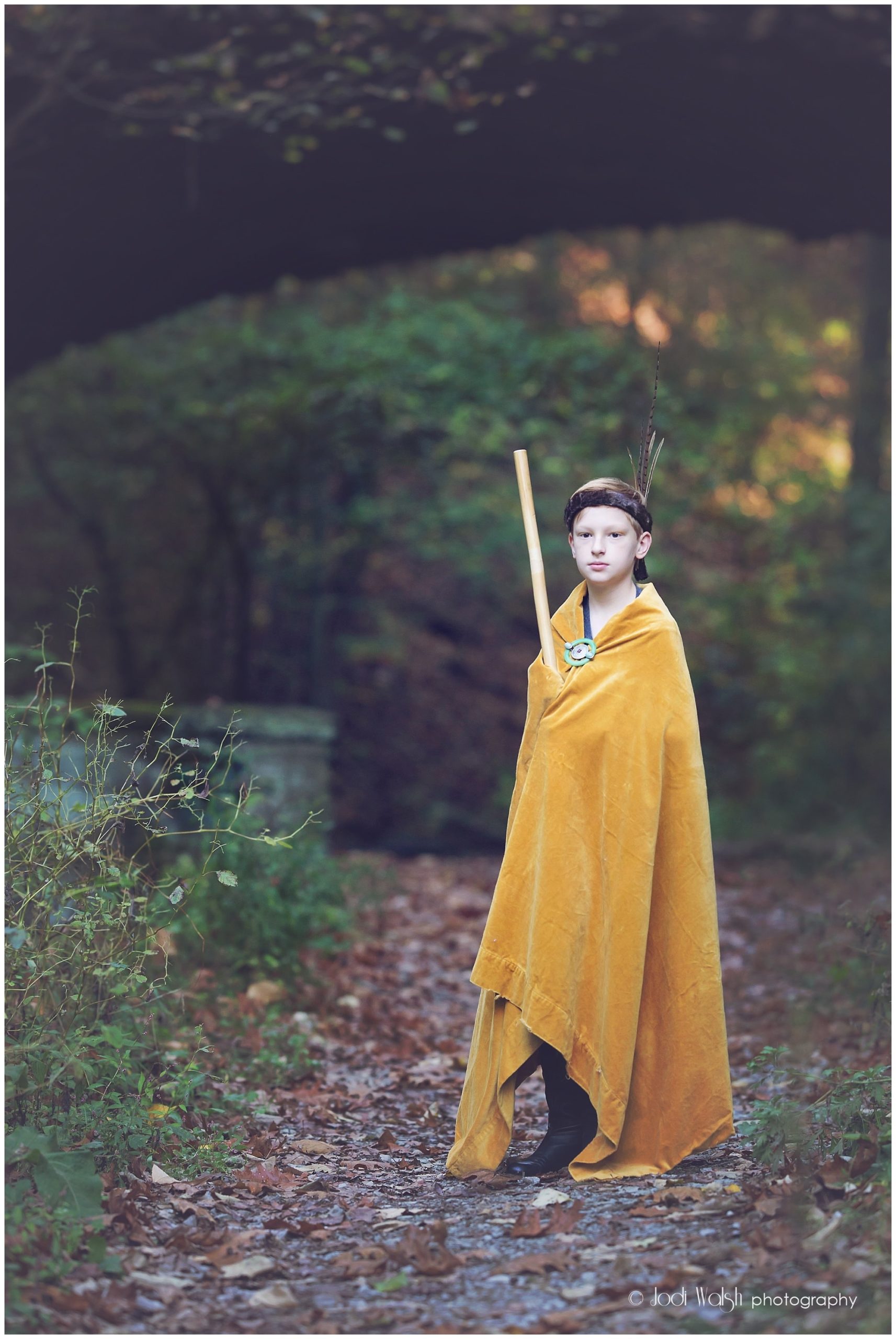 boy with walking stick and yellow cloak in the woods