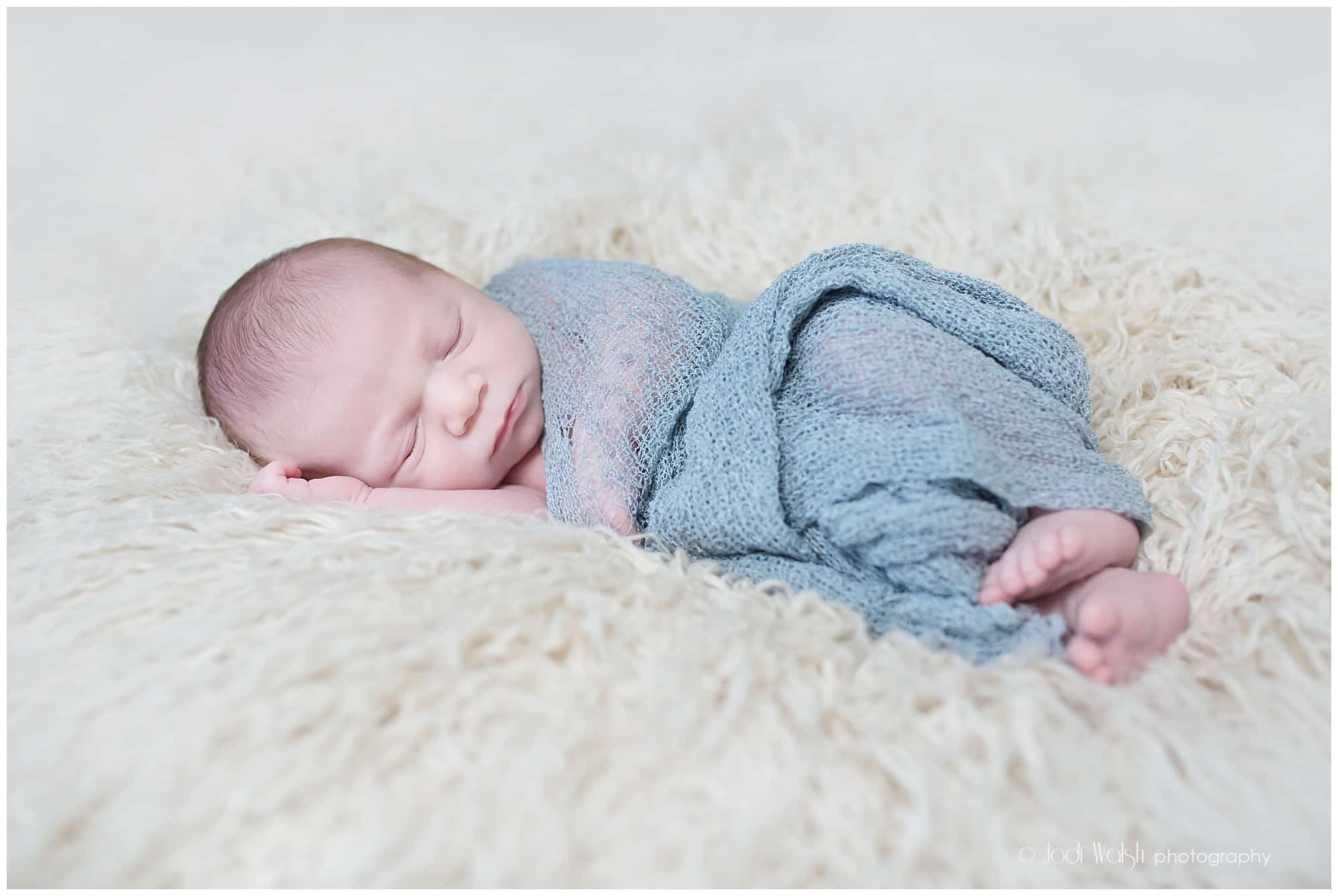 baby boy on cream fur with gray blue wrap