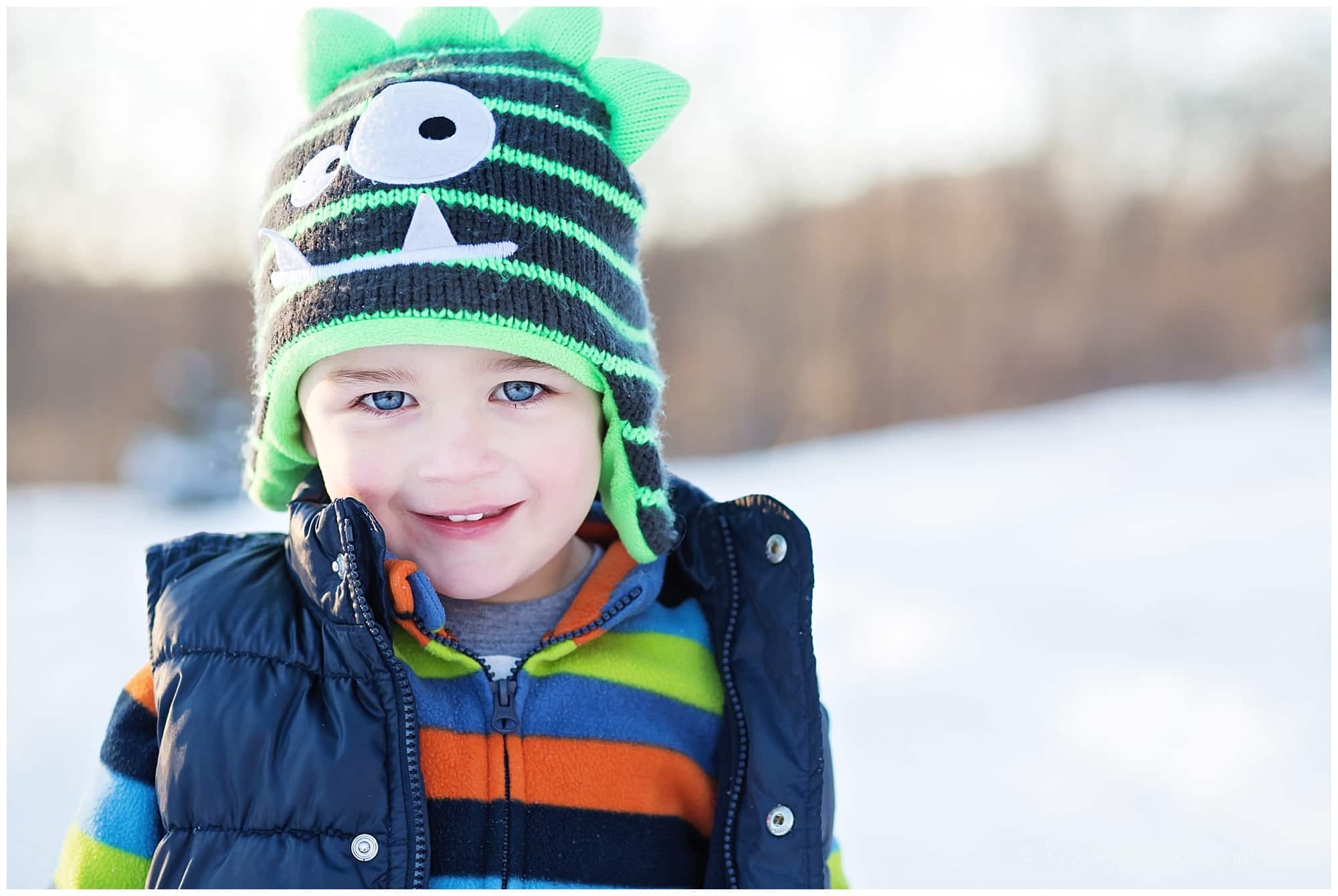 little boy wearing a striped monster hat in the snow