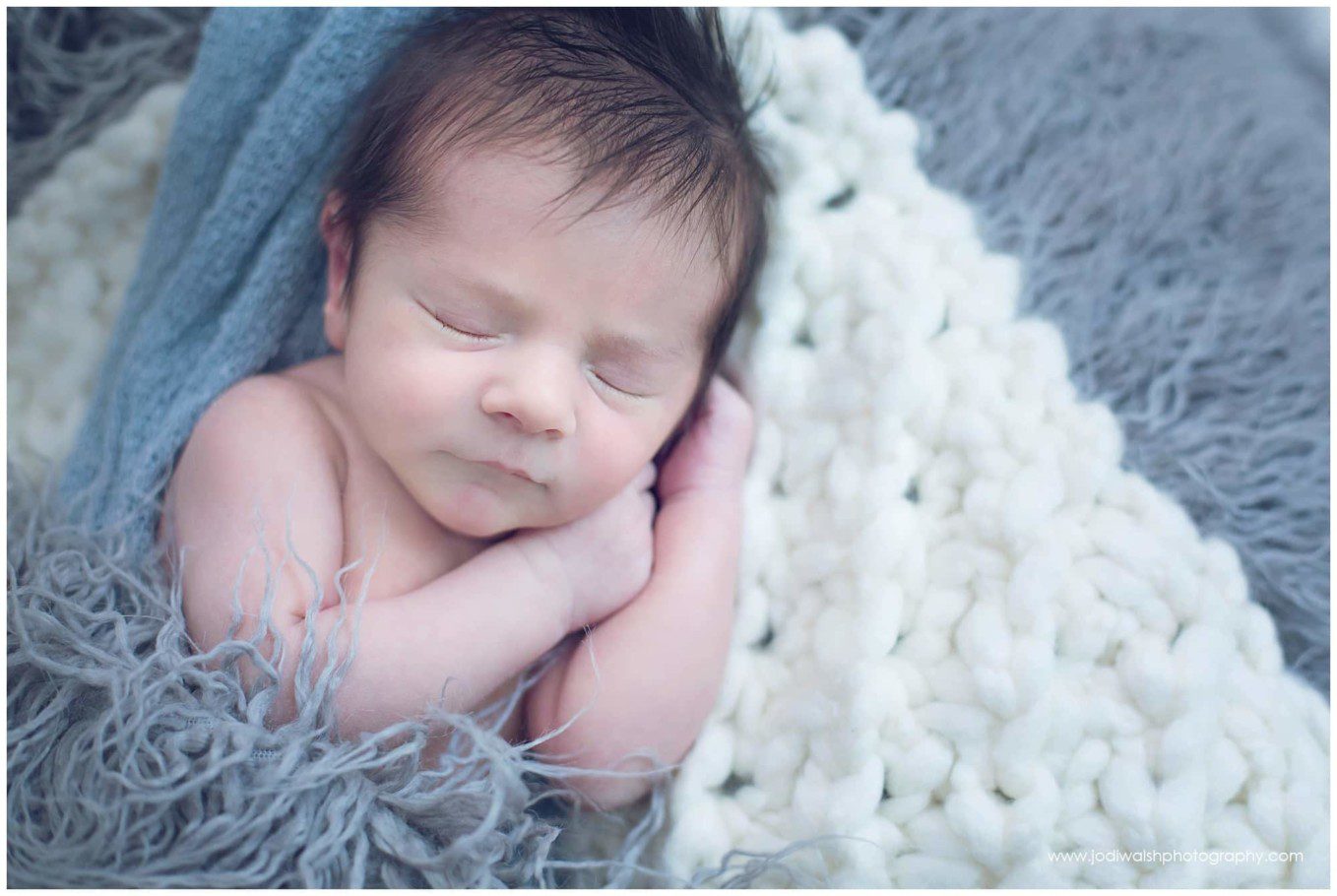 image of a sleeping baby boy. He has a full head of dark hair and is wrapped in blue-gray blankets