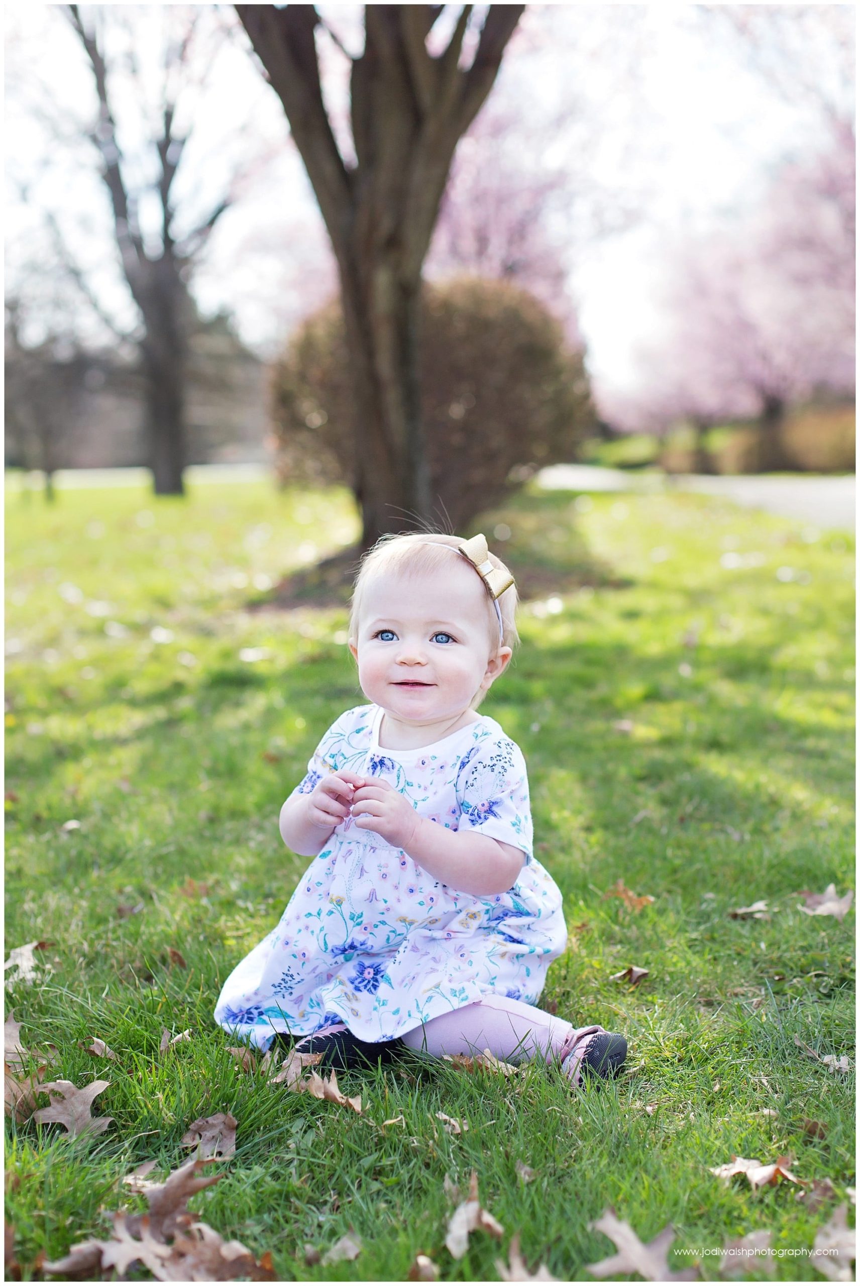 baby girl sitting in the grass wearing blue flowered dress