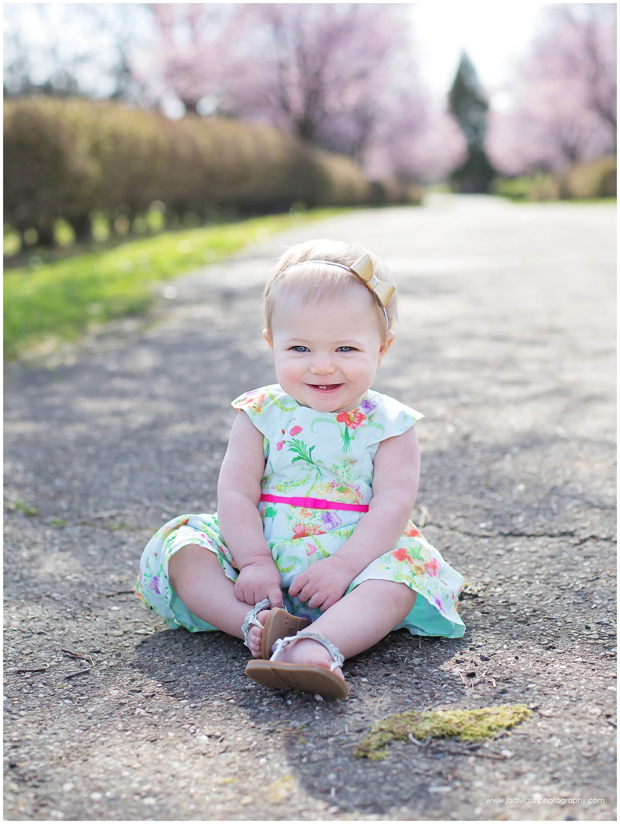 baby girl grinning as she sits in her pink and green dress in a Pittsburgh park in spring