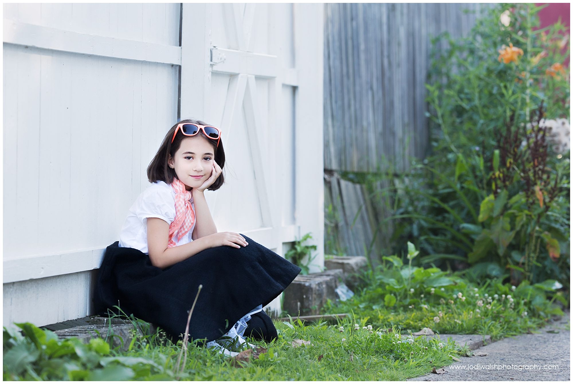 50s girl in poodle skirt sitting in front of a white fence
