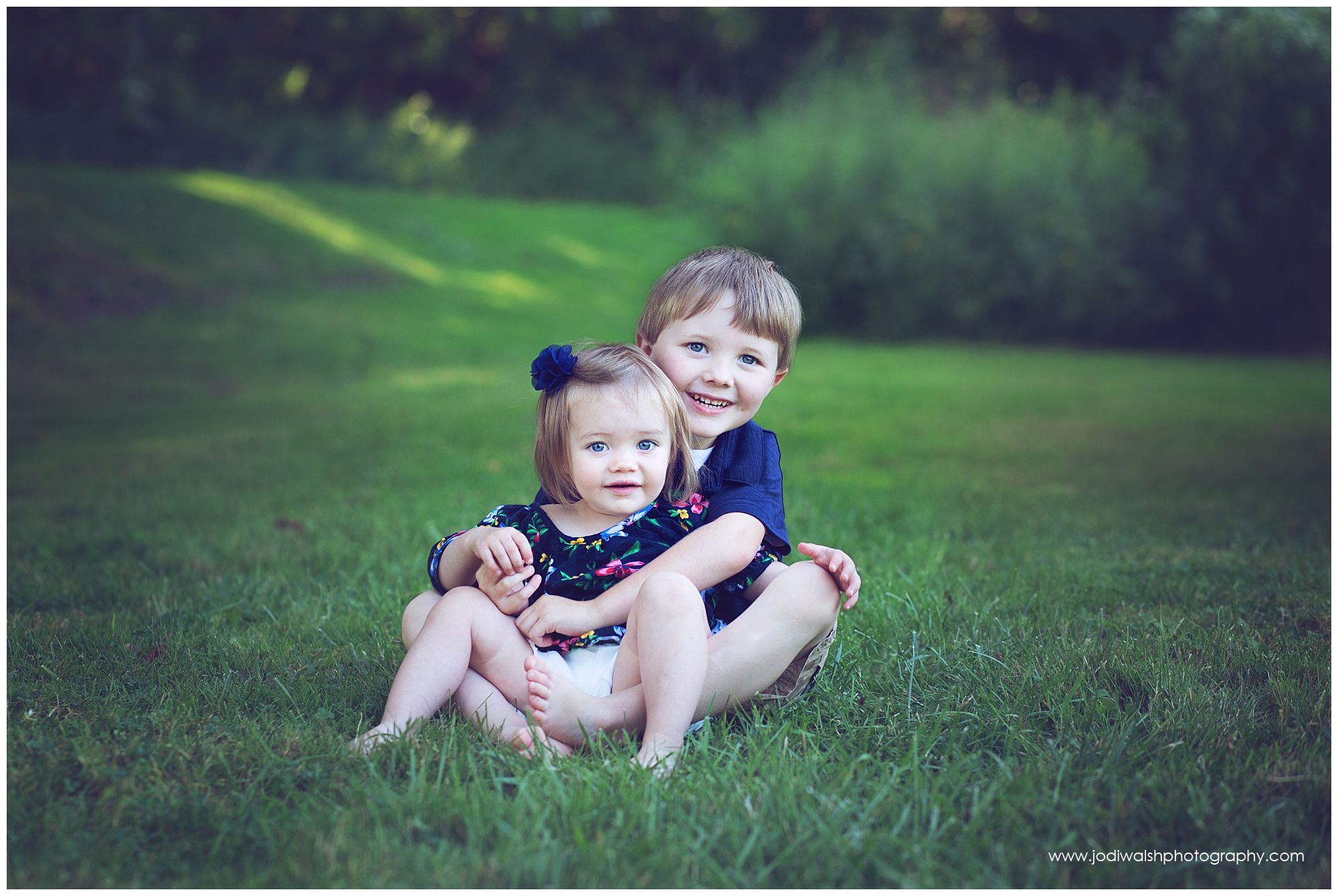 little boy hugging baby sister in the grass at an Erie park in summer