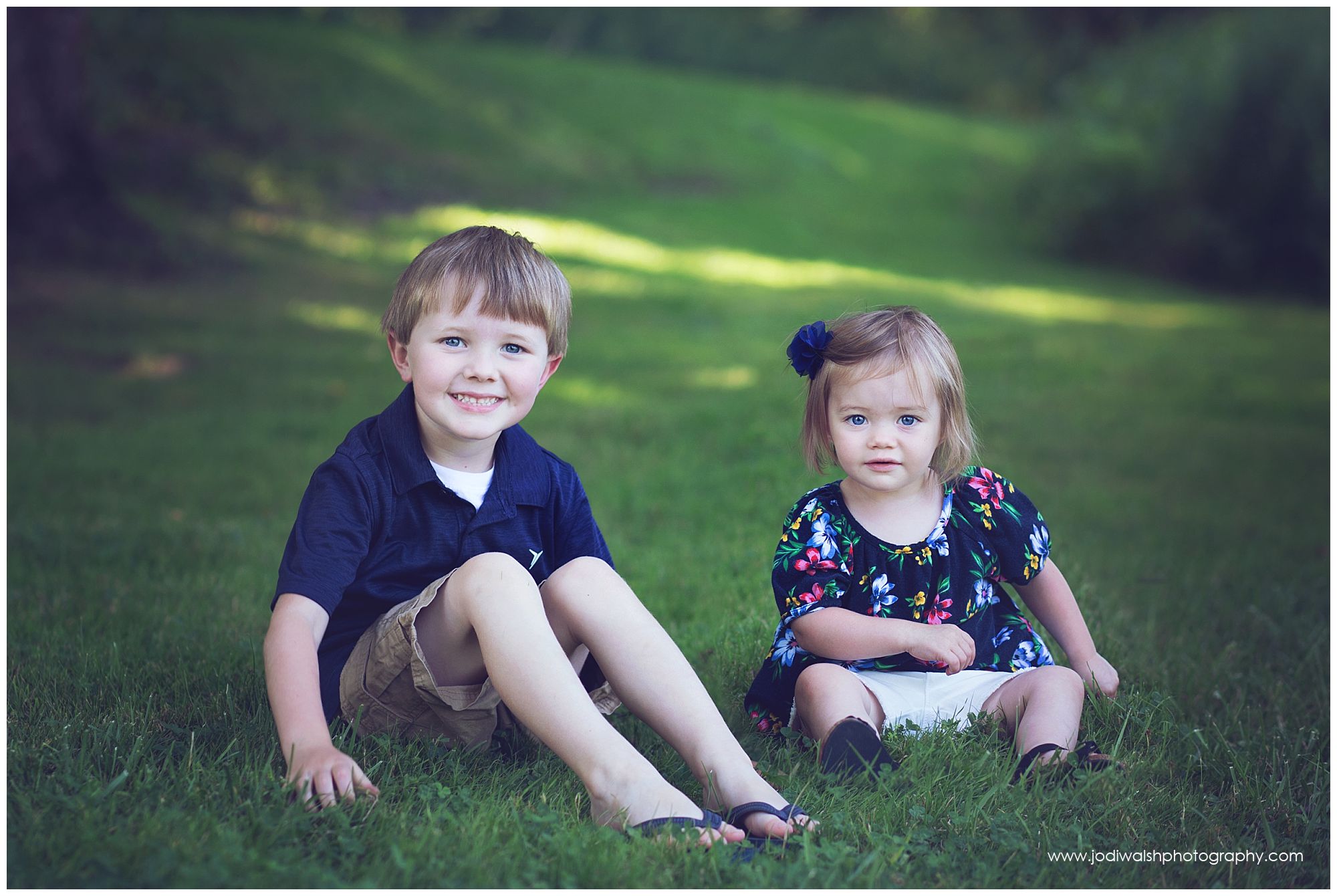 brother and sister in navy blue sitting in the grass at Erie park in summer