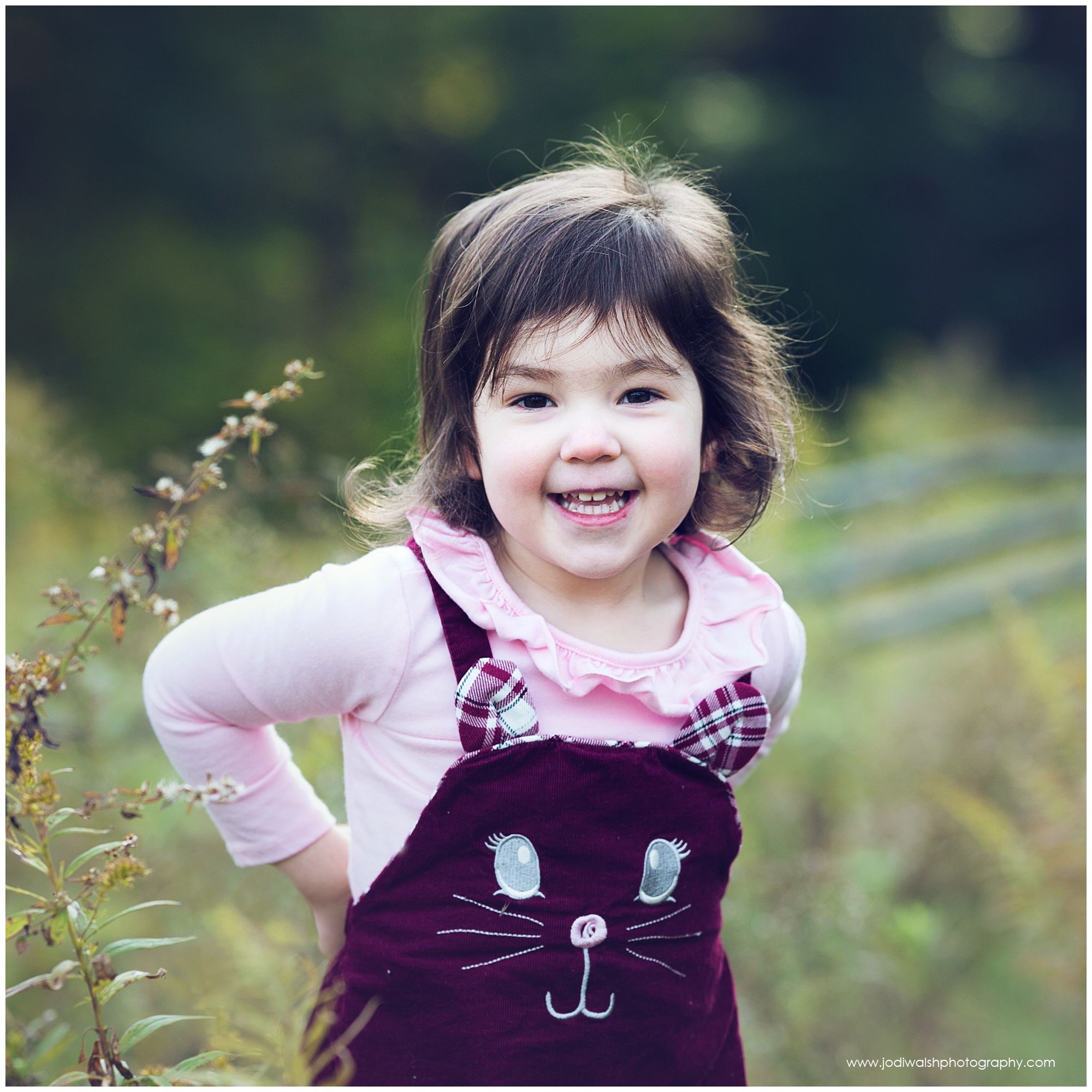 little girl wearing a cat jumper, grinning in the tall grass
