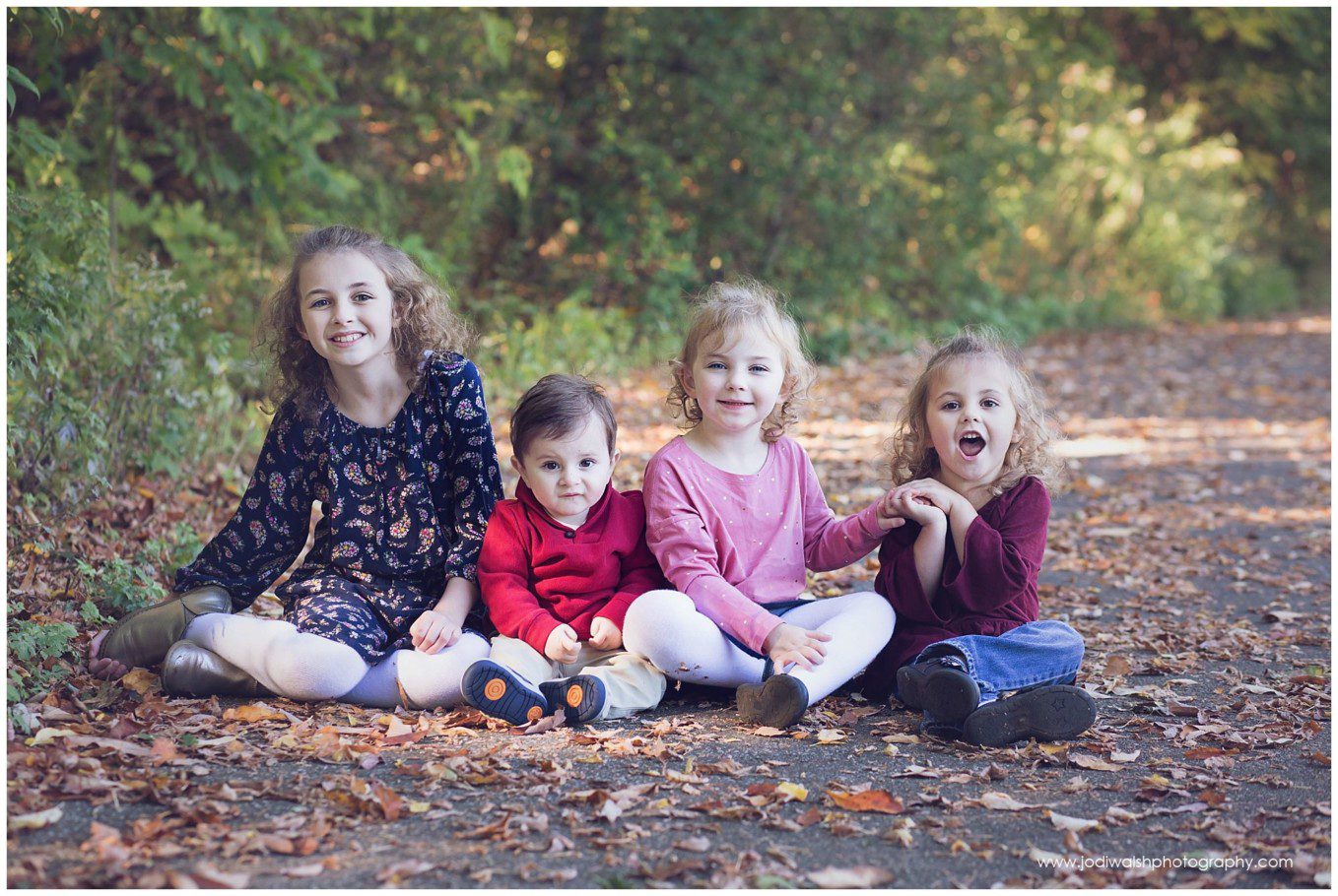 sisters and baby brother sitting in fall leaves in Erie park