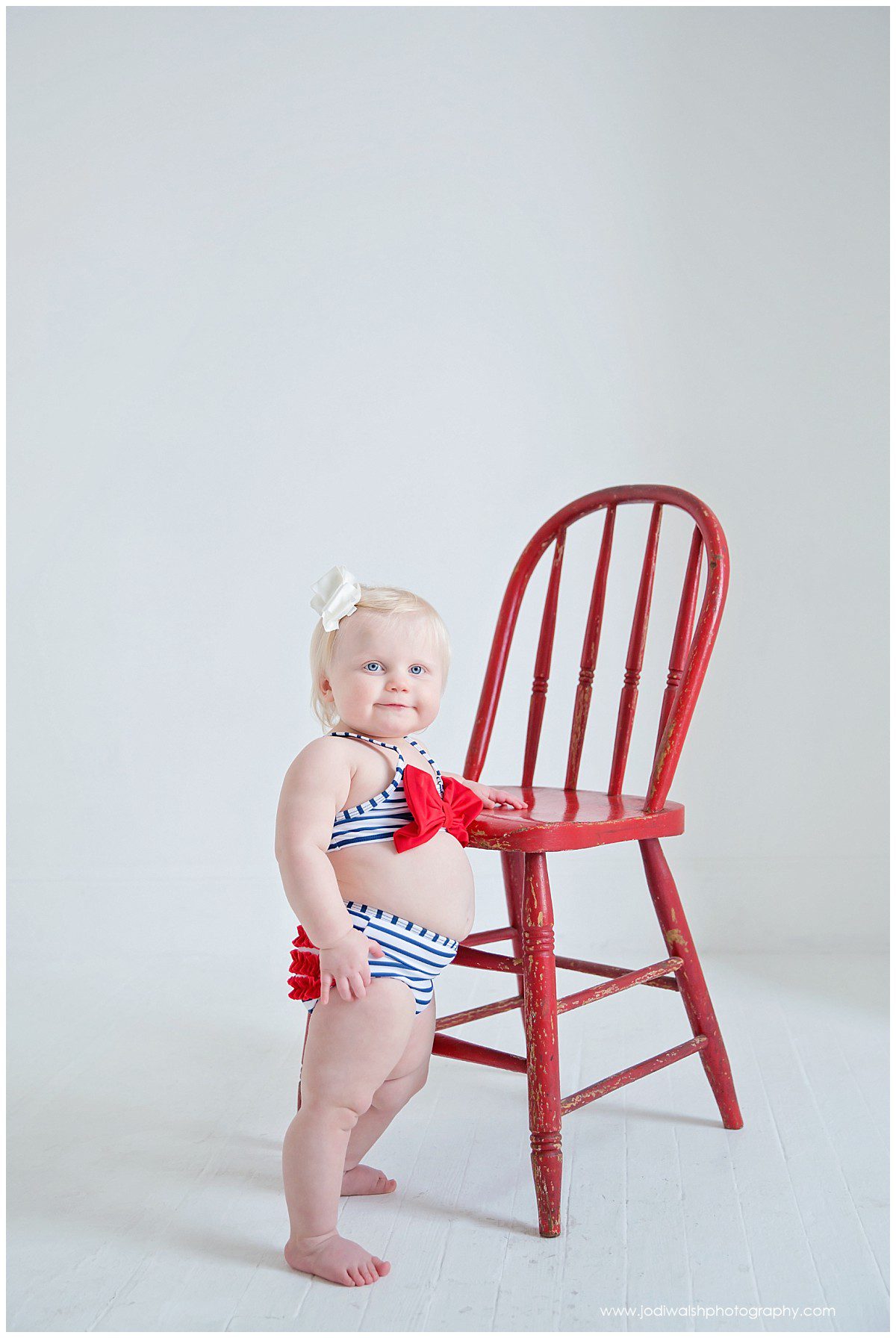 baby girl in bikini standing next to red chair in Pittsburgh studio