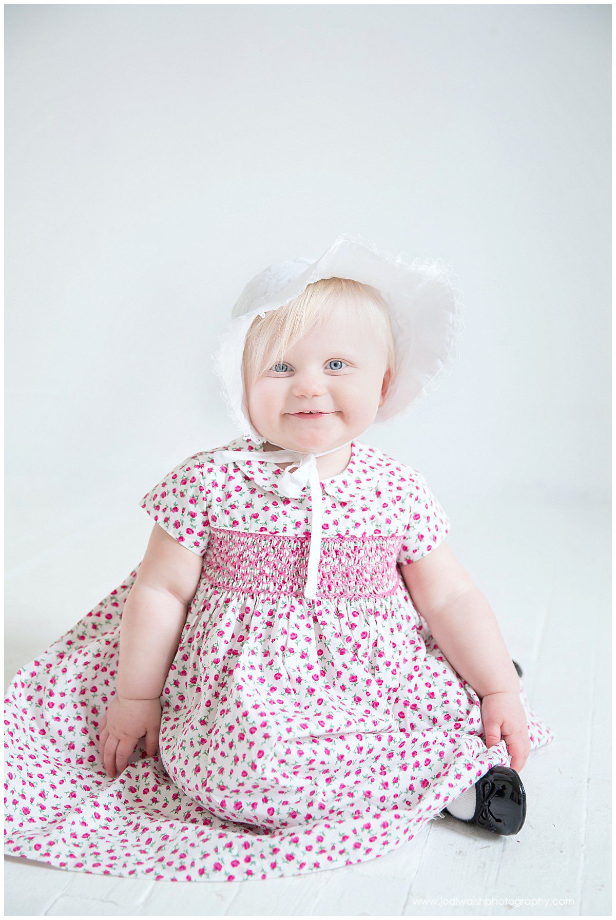 baby girl in pink flower dress and bonnet sitting in Pittsburgh studio