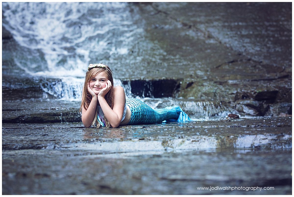 image of a girl laying at the base of a waterfall with her chin in her hands