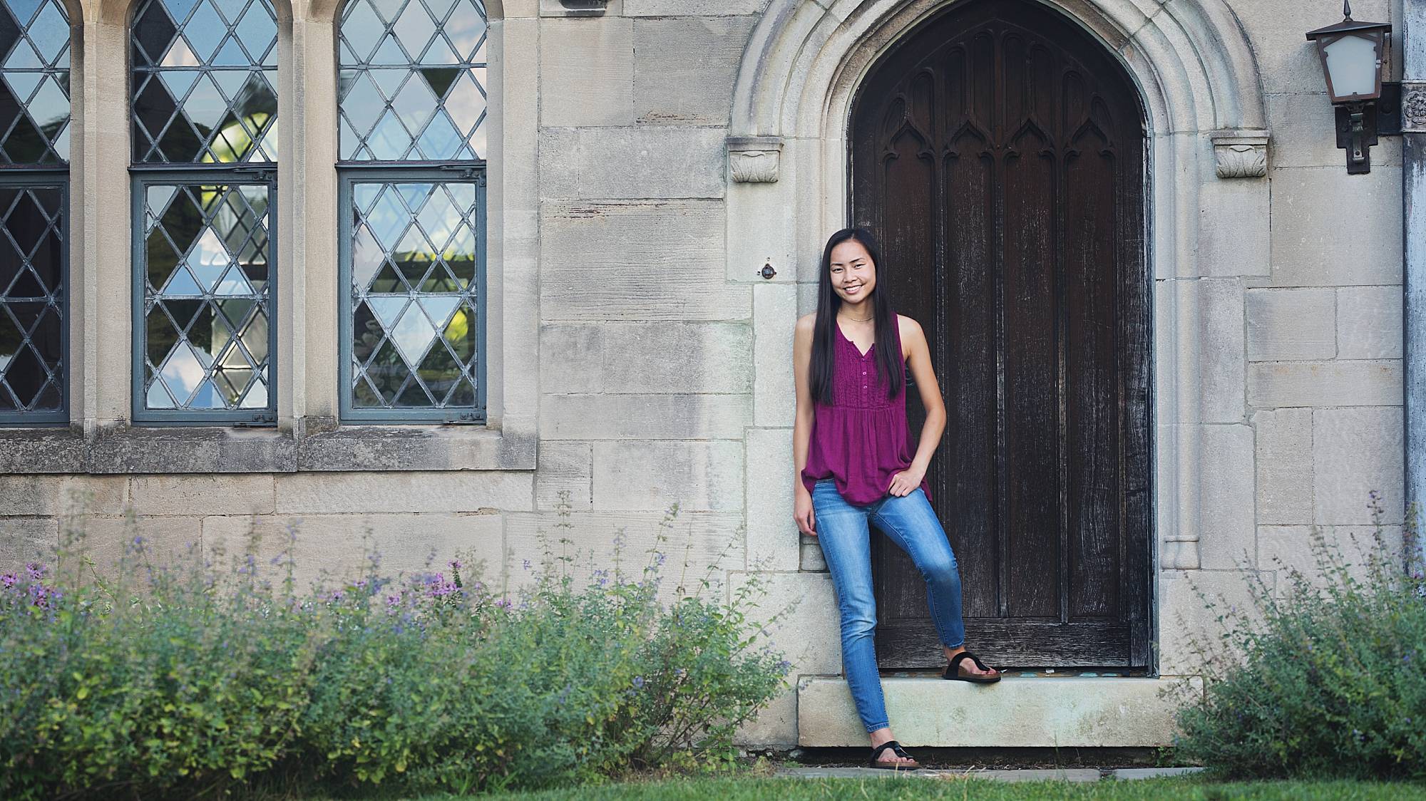 image of a senior girl at Hartwood Acres Mansion. She's wearing a purple top and blue jeans and she's leaning against an old wooden door.