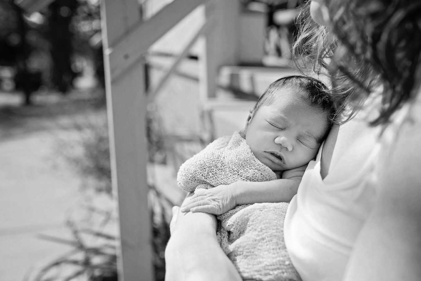 close up black and white image of a mother sitting on a front step, holding her newborn close to her chest