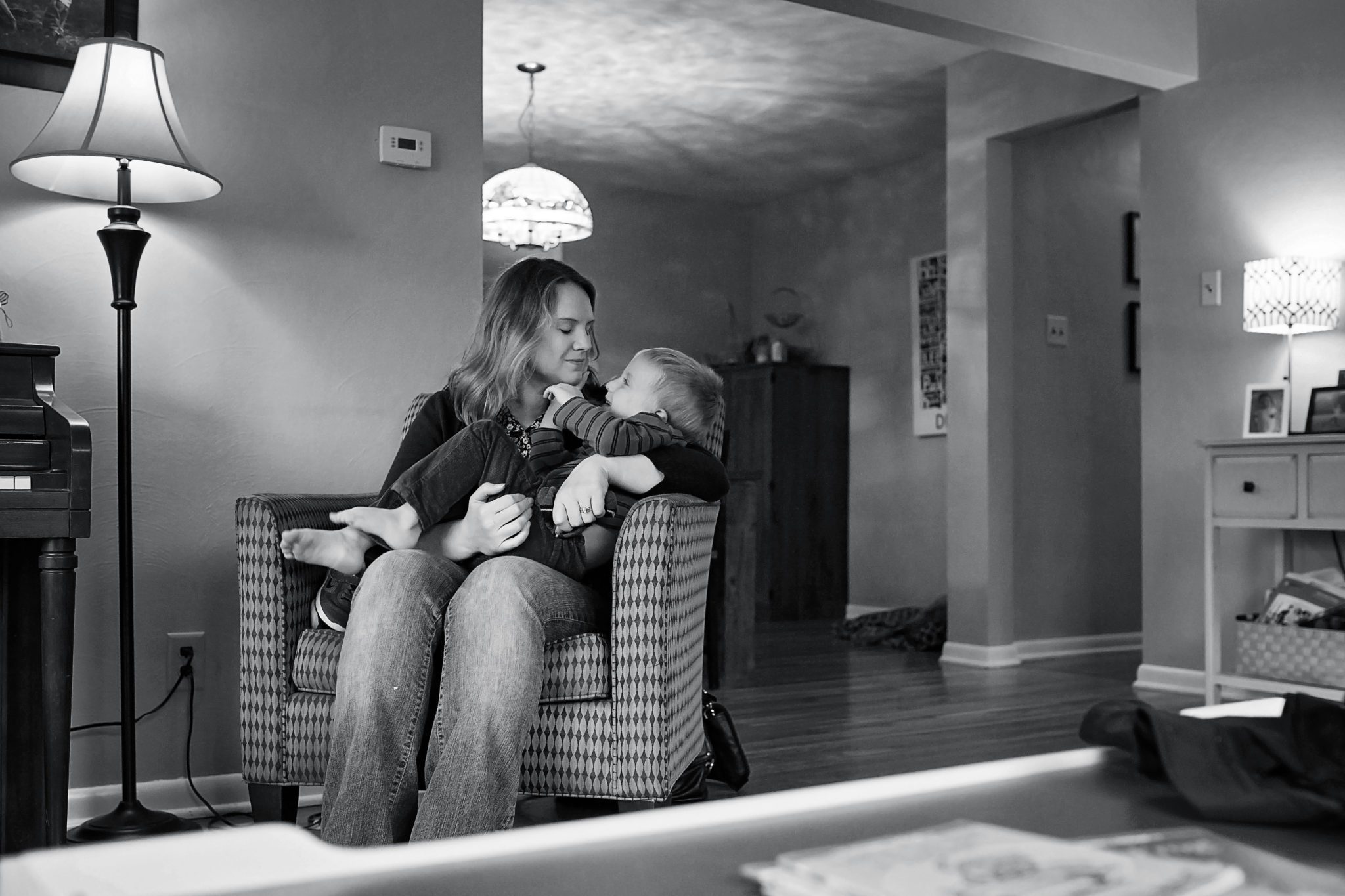black and white image of a mom sitting in an armchair in a living room, cradling her son