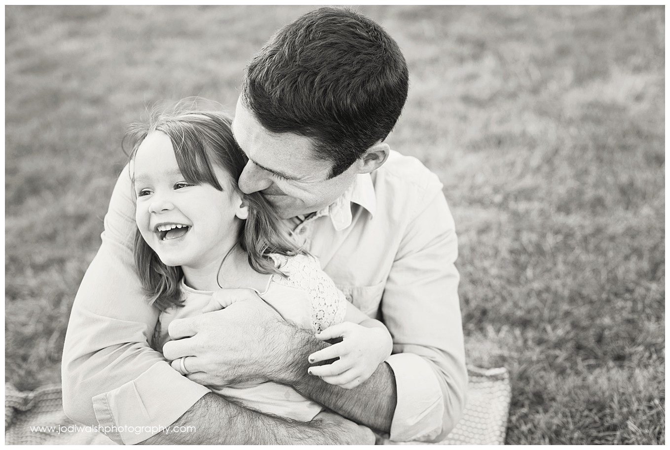 black and white image of a dad hugging his little girl. He's looking down and smiling and she's looking up and grinning.