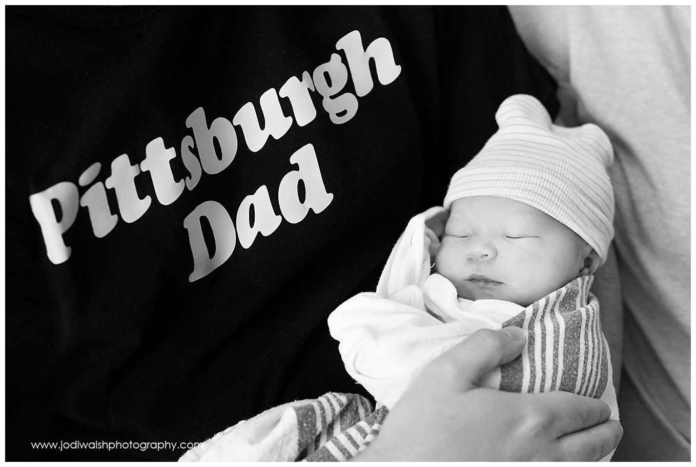 black and white image of a father wearing a Pittsburgh Dad t-shirt cradling his newborn baby.