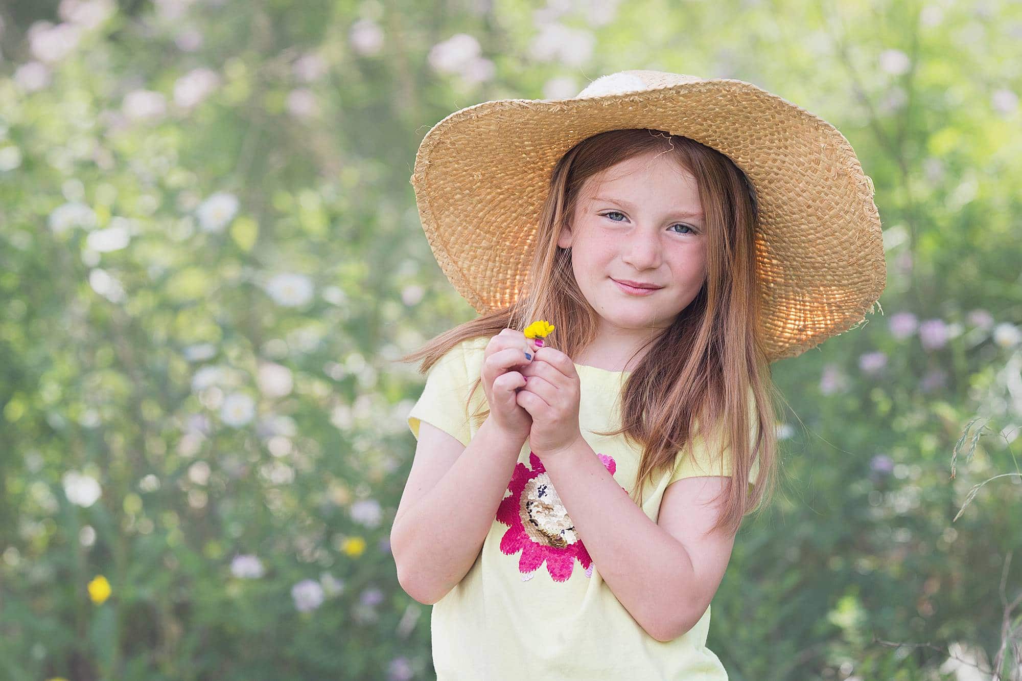 little girl with red hair in a straw hat with wildflowers