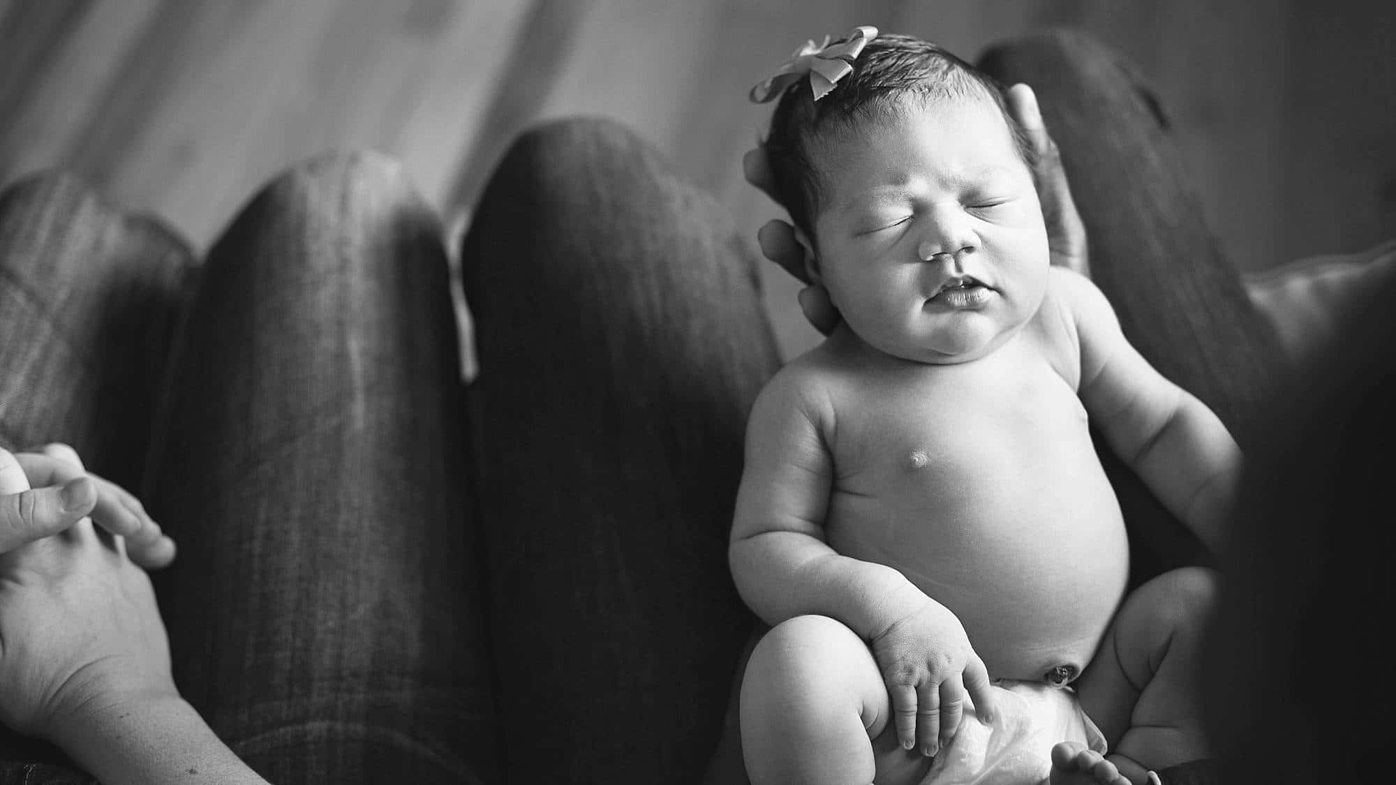 black and white image of a newborn baby girl being held in father's lap in a Pittsburgh home