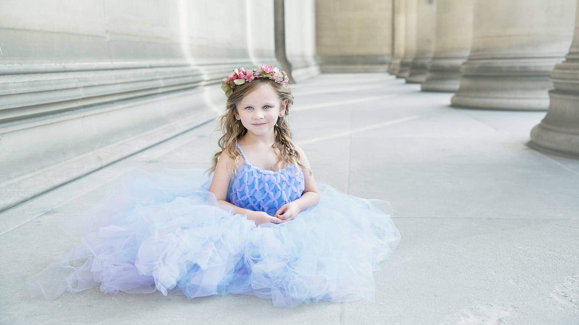 image of a little girl, sitting in a marble hall with columns wearing a light blue tulle dress