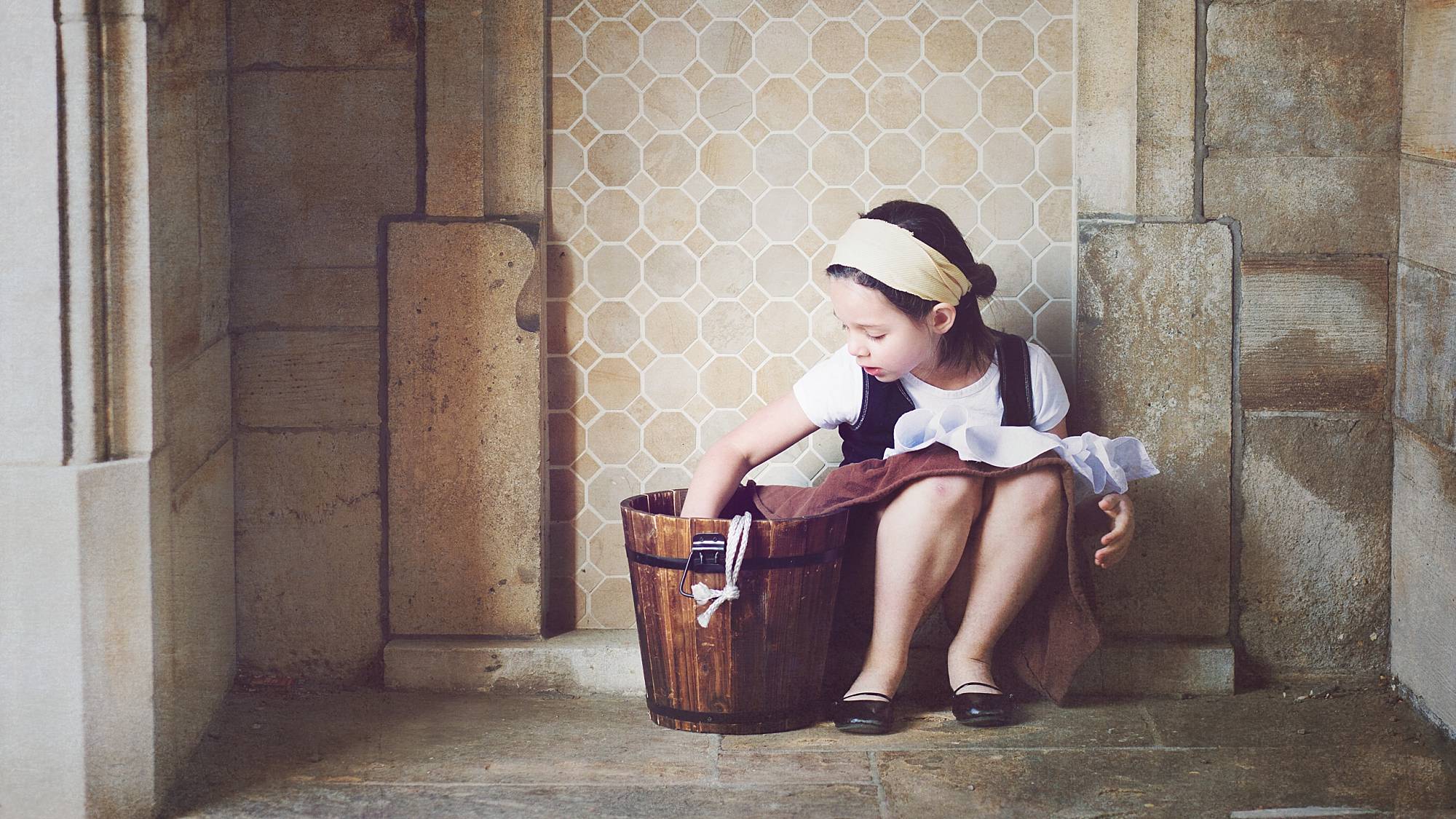 image of a little girl in a stone alcove, dressed as Cinderella washing the floors