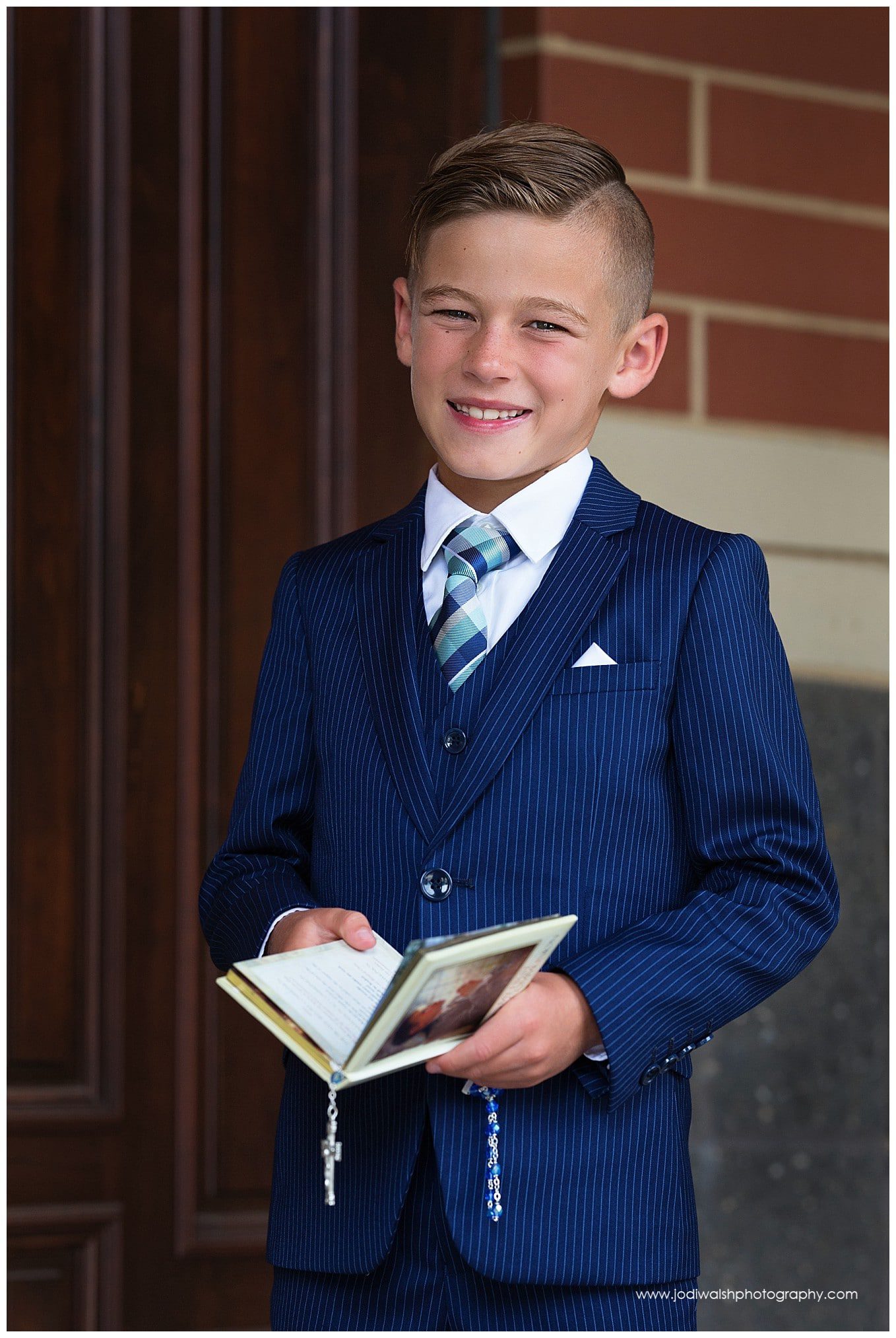 image of a young boy wearing a blue suit holding a prayer book for his first holy communion