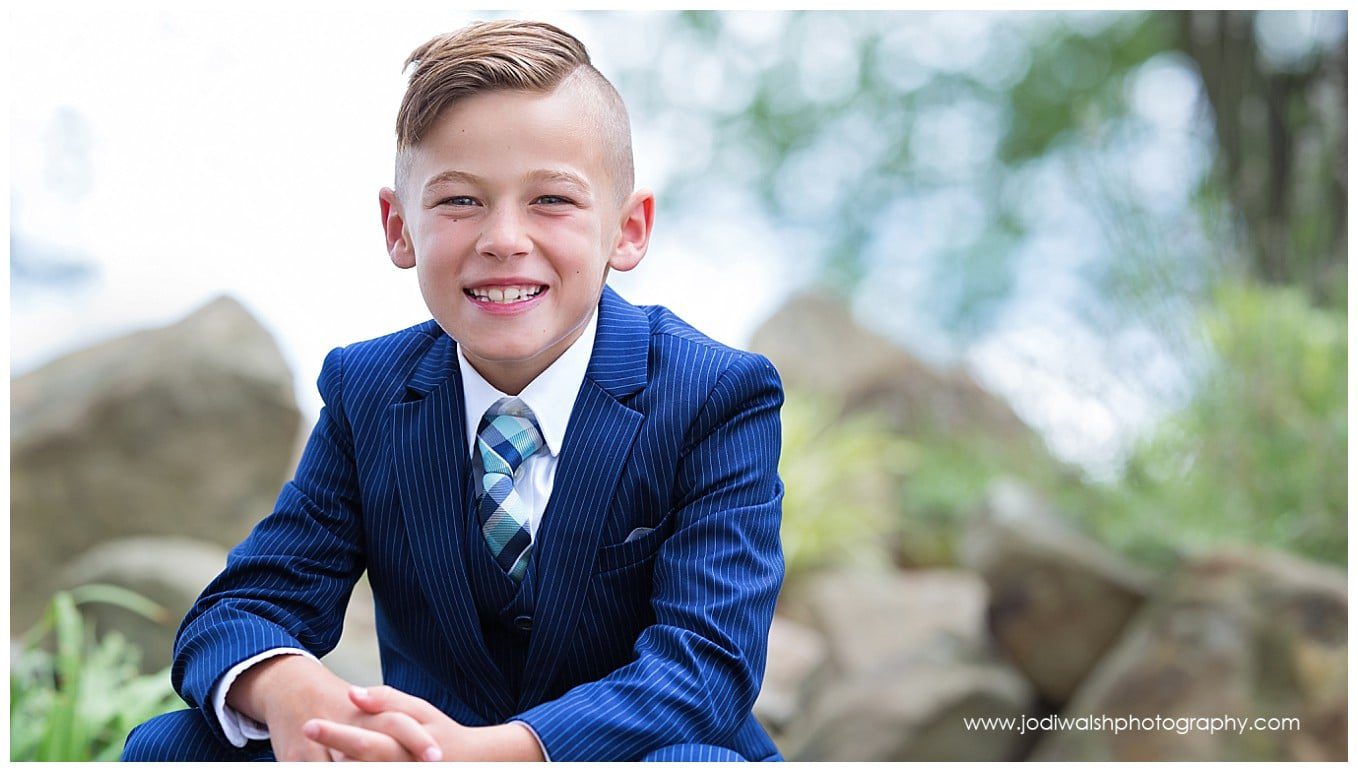 closeup image of a young boy wearing a blue suit, with rocks and trees in the background