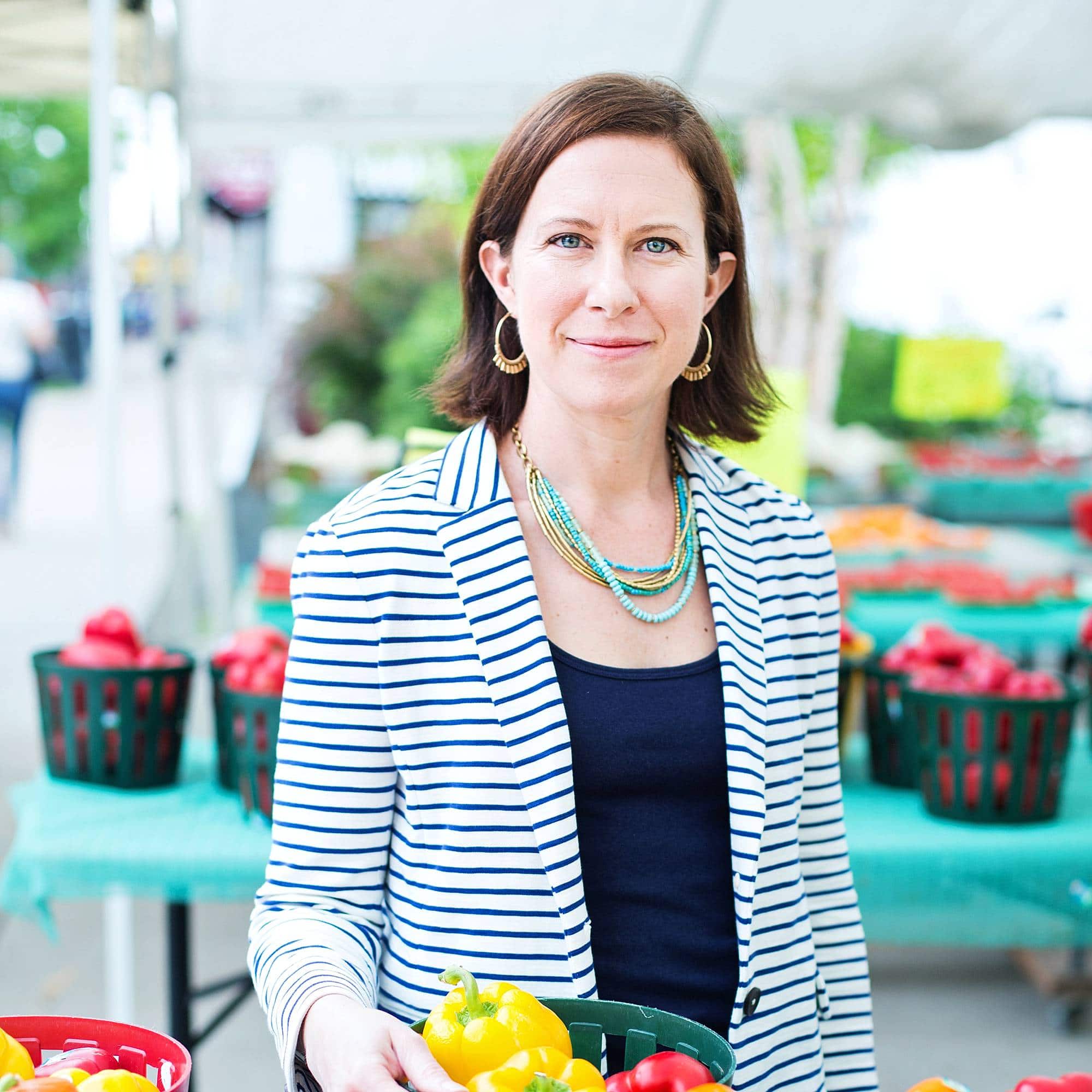 image of a woman wearing a striped jacket standing under a white tent farm stand