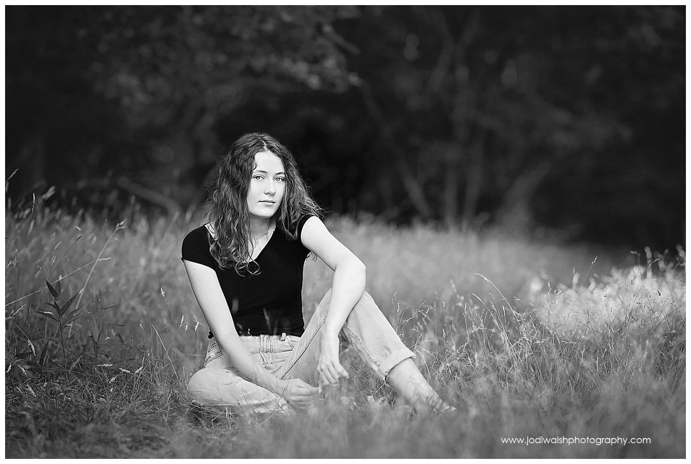 black and white image of a senior girl in North Park.  She's wearing blue jeans and a black t-shirt and she's sitting in a field of tall grass.
