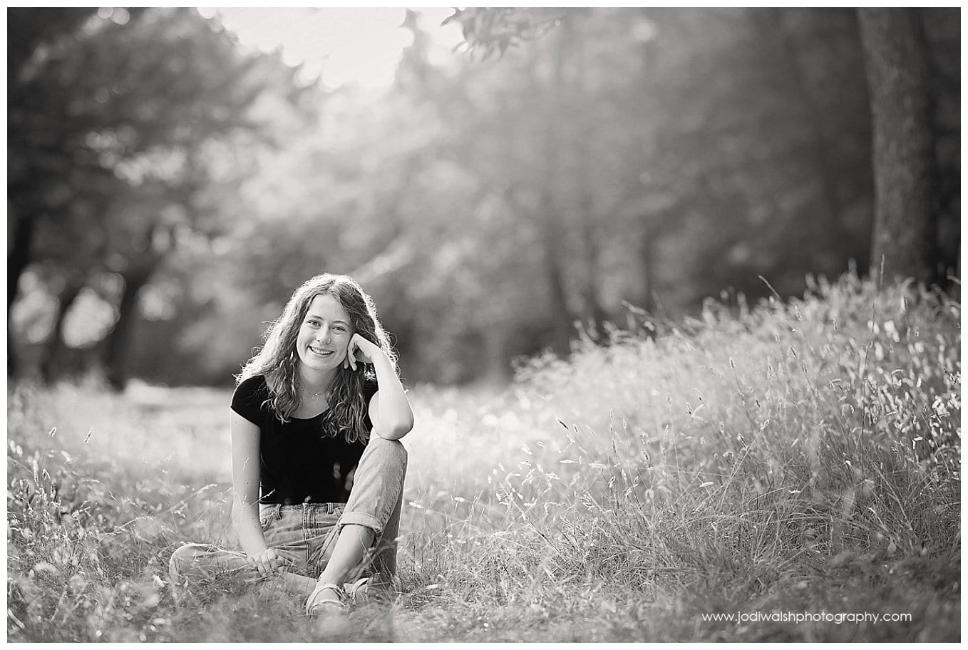 black and white image of a senior girl sitting in a field of tall grass in North Park.  She has her elbow resting on her knee with her hand by her cheek.