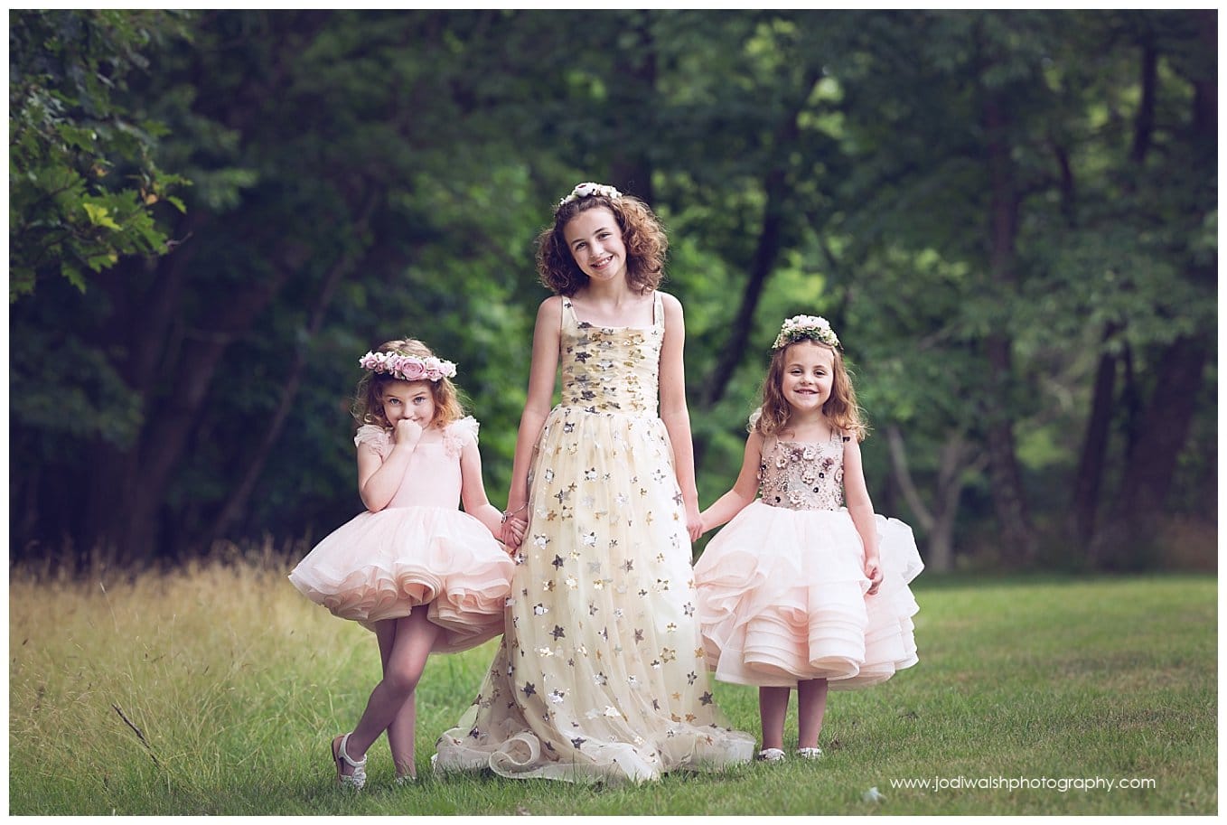 image of three little sisters wearing princess dresses and holding hands while standing in a clearing in North Park.