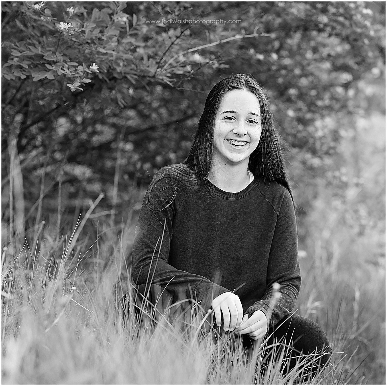 black and white image of a teen girl sitting in tall grasses smiling