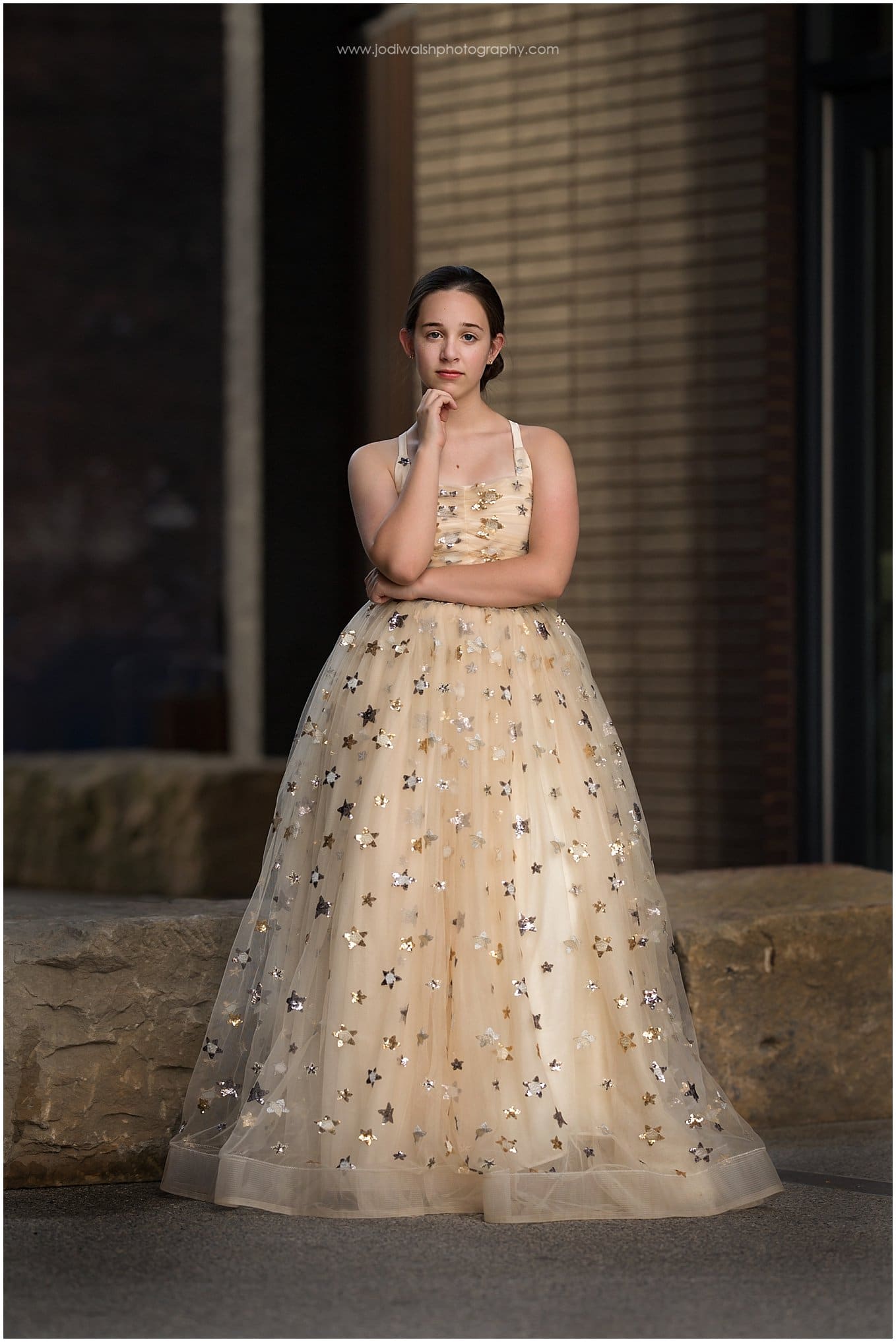image of a teen girl in a gold princess dress with silver stars. She's standing in a Pittsburgh alley with her arms crossed, looking serious.