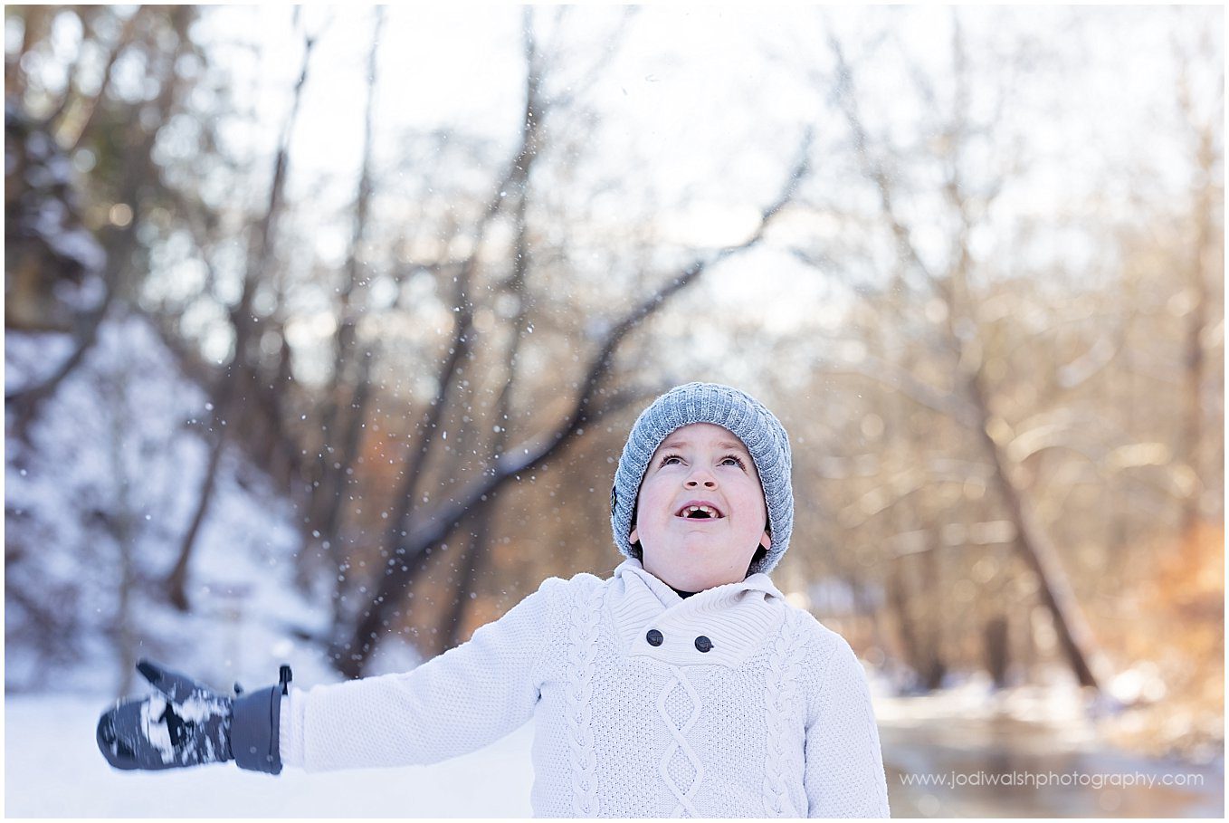 image of a little boy in a white sweater and gray knit hat tossing snow over his head