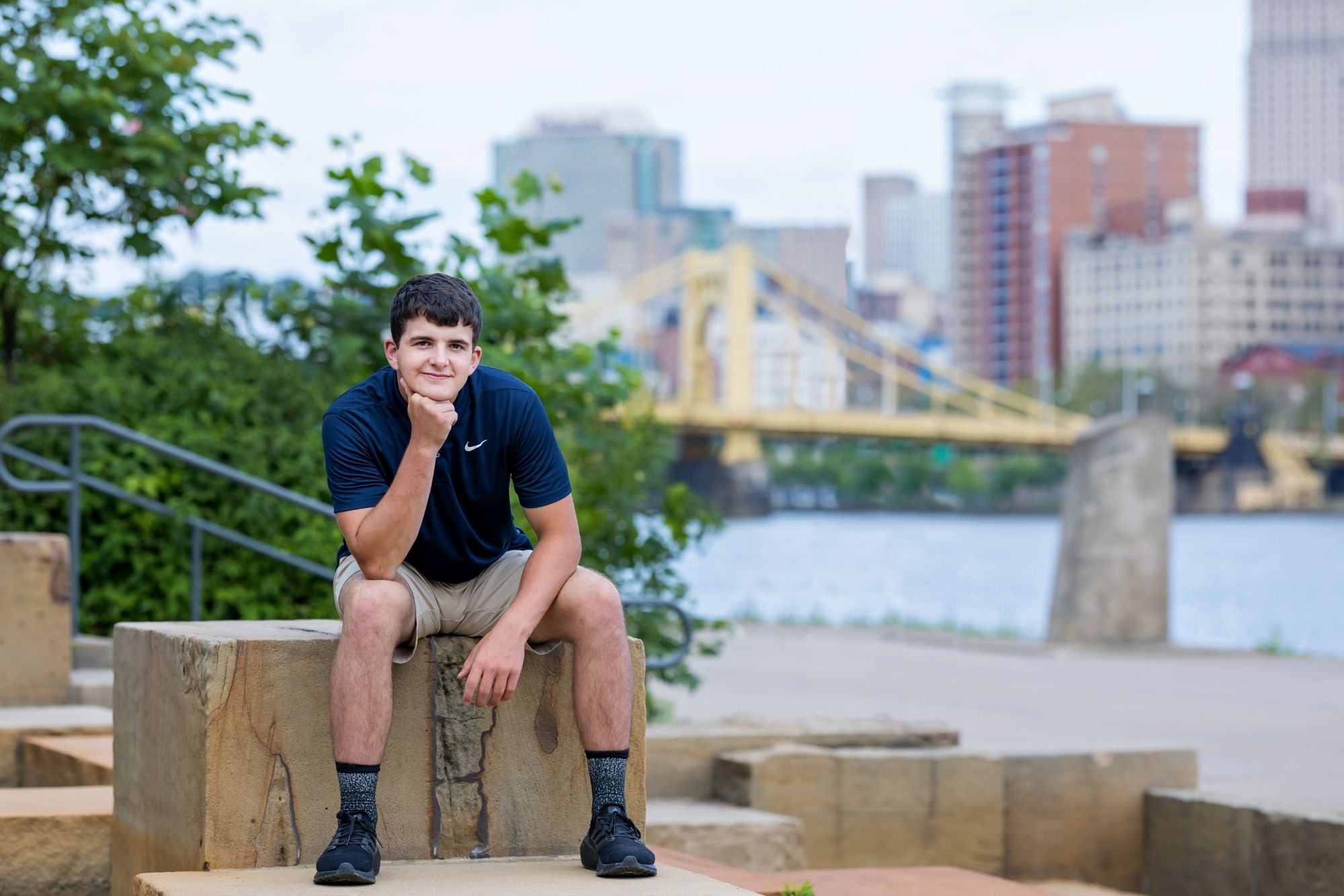 senior guy sitting on the watersteps in Pittsburgh. The Clemente Bridge is in the background.