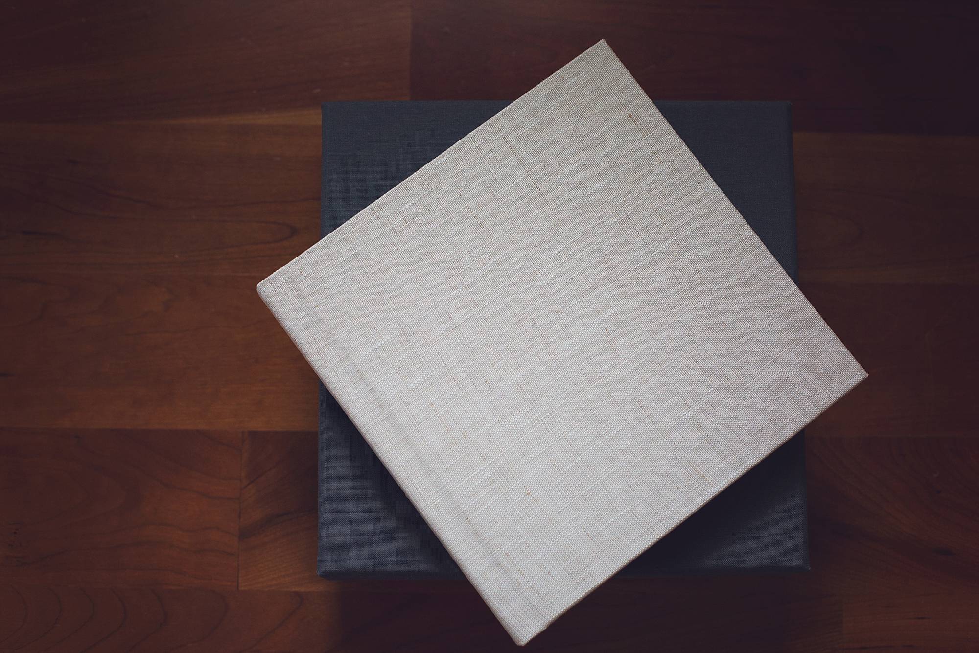 image of a square linen covered photo album. the cover is beige and the album is set on a dark wood floor