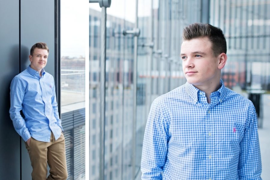 two images of a senior guy in a glass atrium. He's wearing a light blue dress shirt and tan pants. He's looking out of the window at the city buildings below.