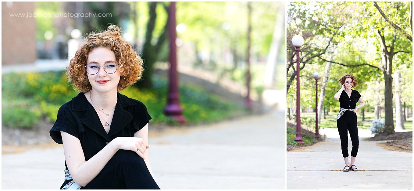 senior girl wearing a black jumpsuit on a sidewalk at Indiana University of Pennsylvania. She's has short, curly, red hair and wire-rimmed glasses.