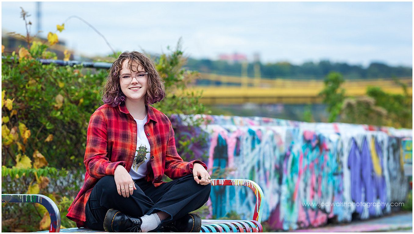 senior girl wearing a red plaid shirt and sitting on a graffiti covered bench at the Color Park, Pittsburgh