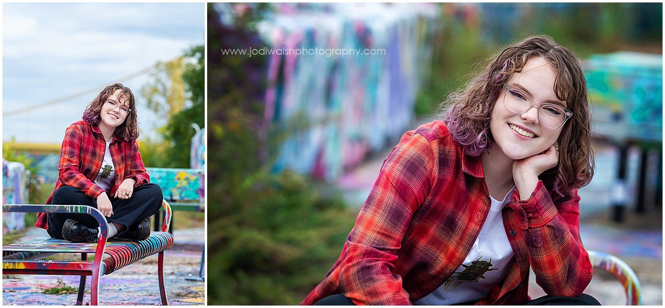 senior girl sitting on a graffiti covered bench at the Color Park, Pittsburgh. She's wearing black jeans and a red plaid shirt.