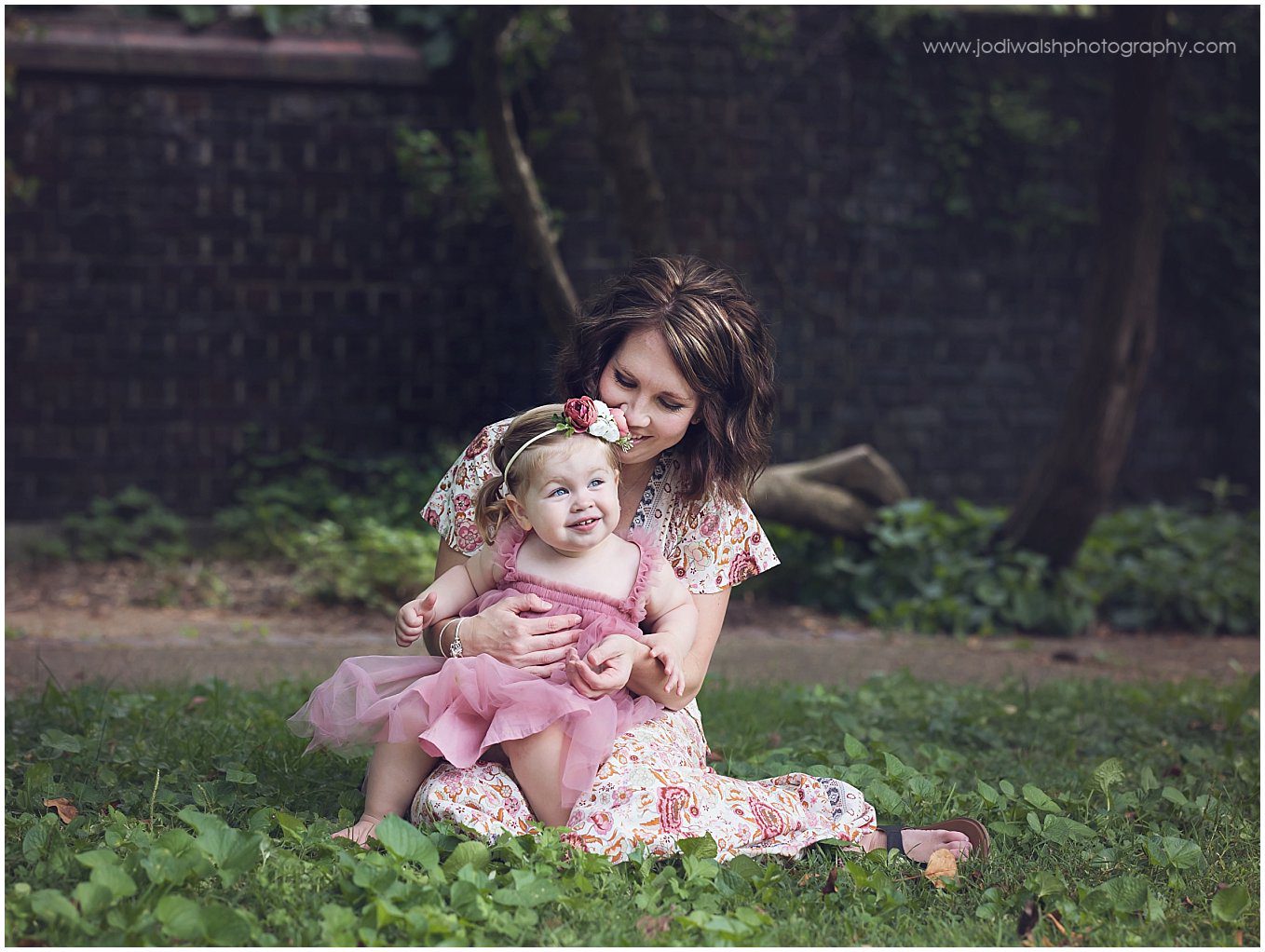 image of a mother holding her young daughter in her lap while sitting in a walled garden at Mellon Park.