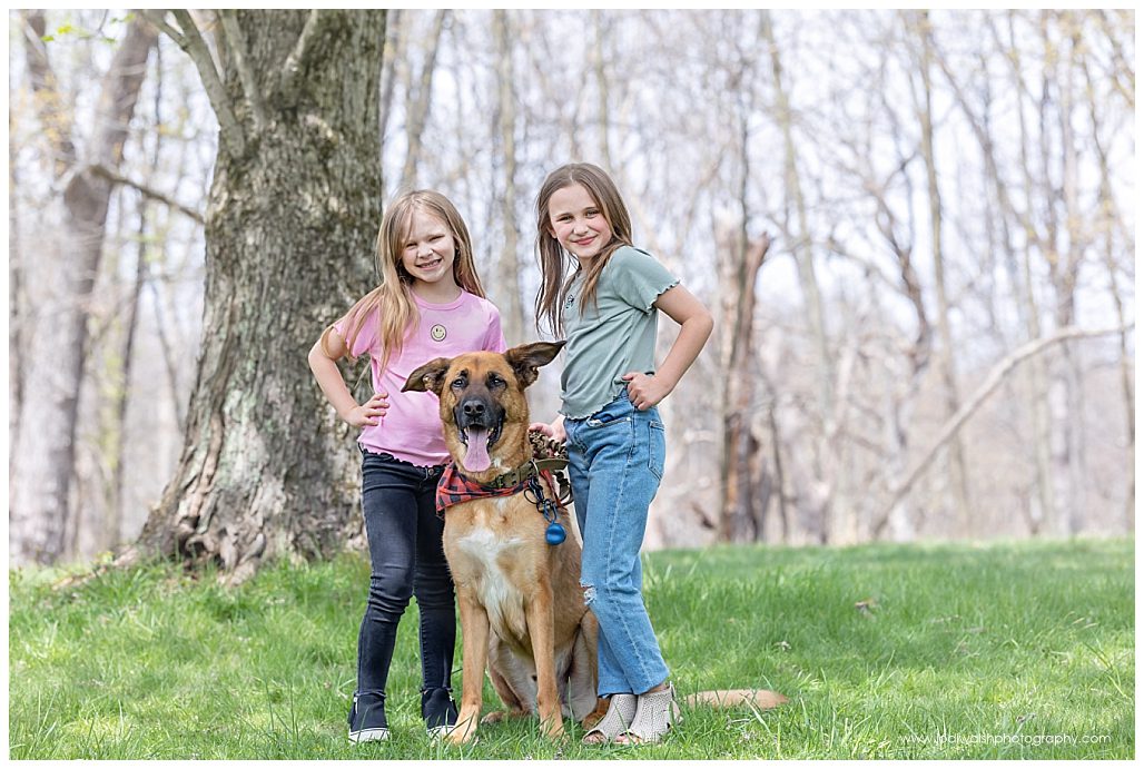 image of little girls standing in North Park with their dog. The dog is a large and brown with black ears that flop.